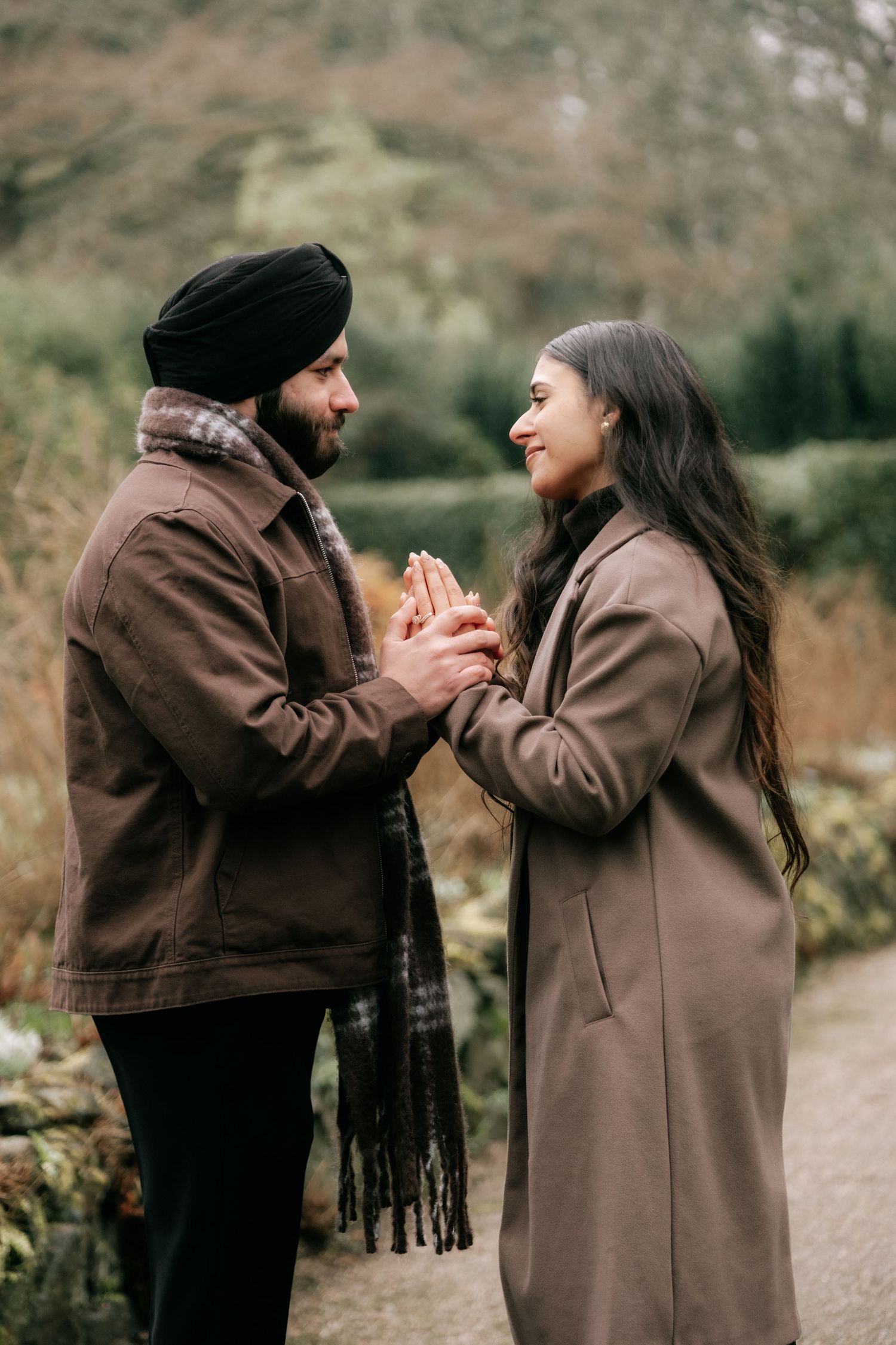 A couple shares an intimate moment while holding hands in a winter garden.