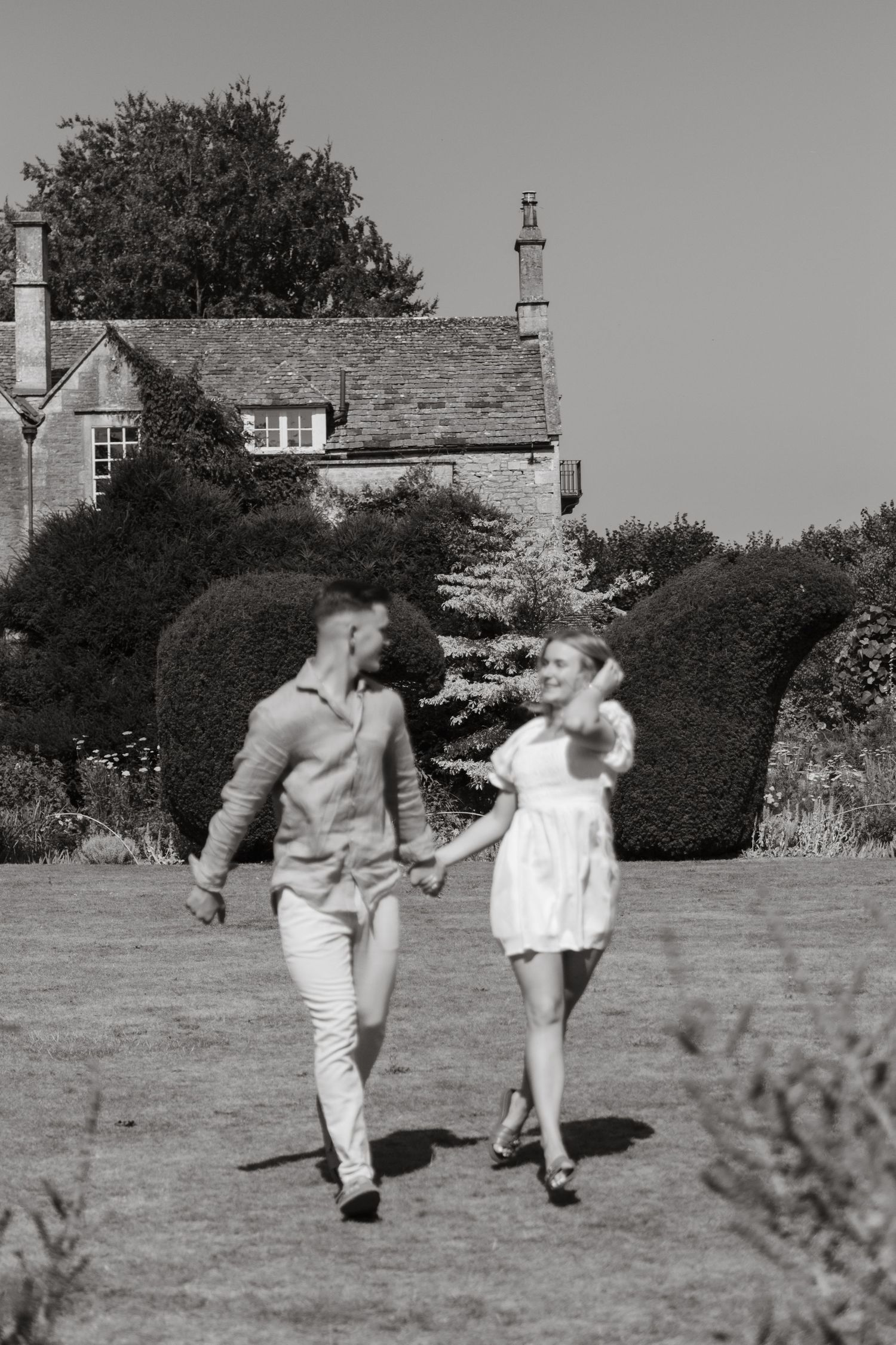 A couple dances playfully across a grassy field in black and white.