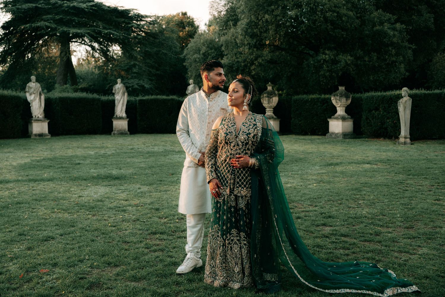 Wedding couple walking through garden with flowing emerald green cape.