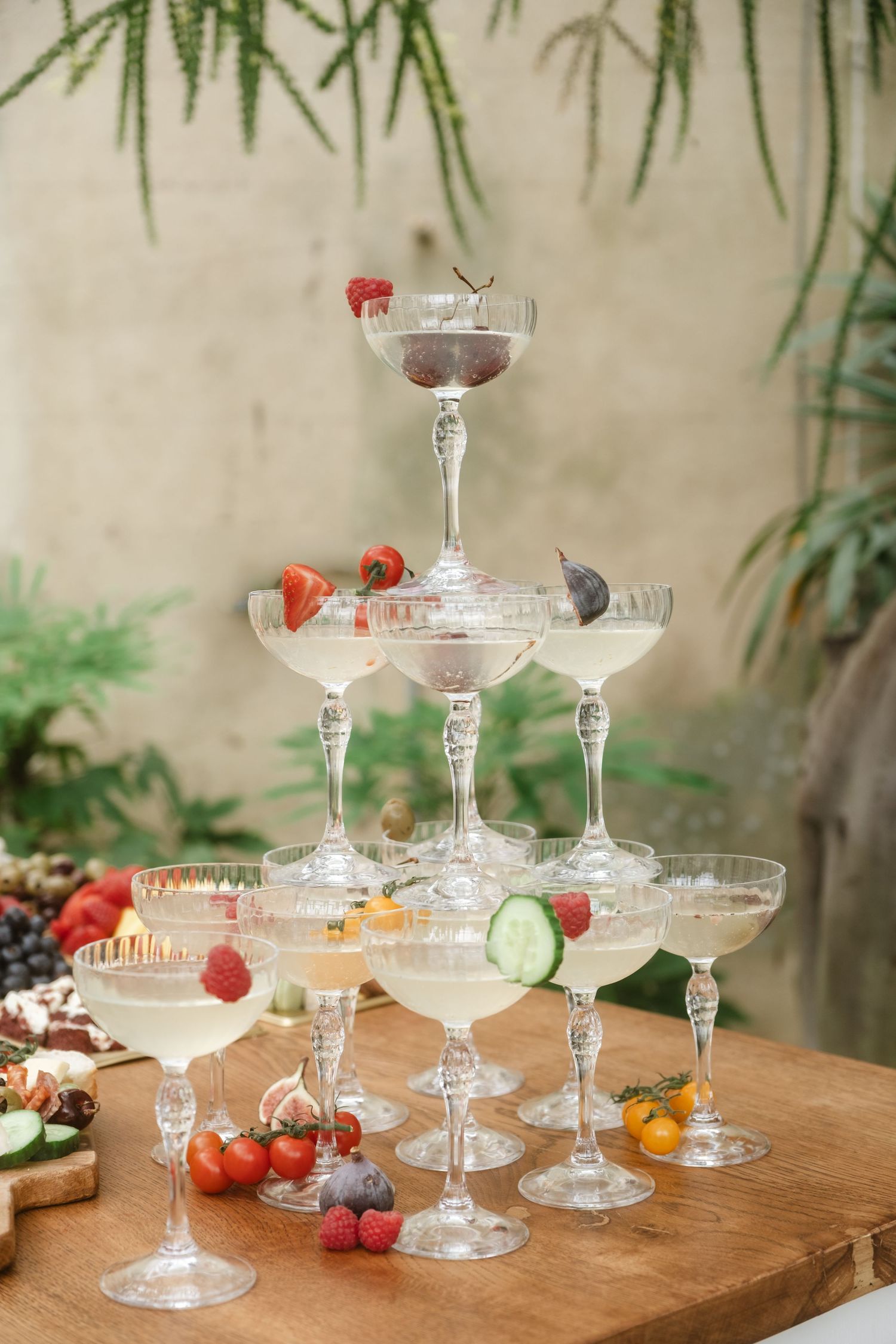 Vintage-style champagne coupe glasses arranged on a wooden table with fresh fruits and garnishes.