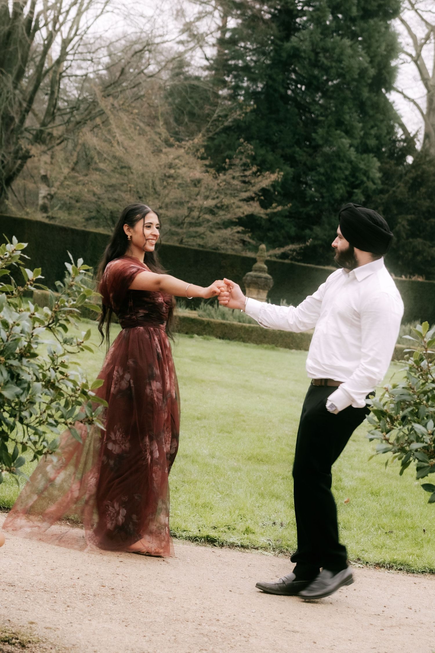 A couple dances together on a garden path, with her wearing a flowing burgundy dress.