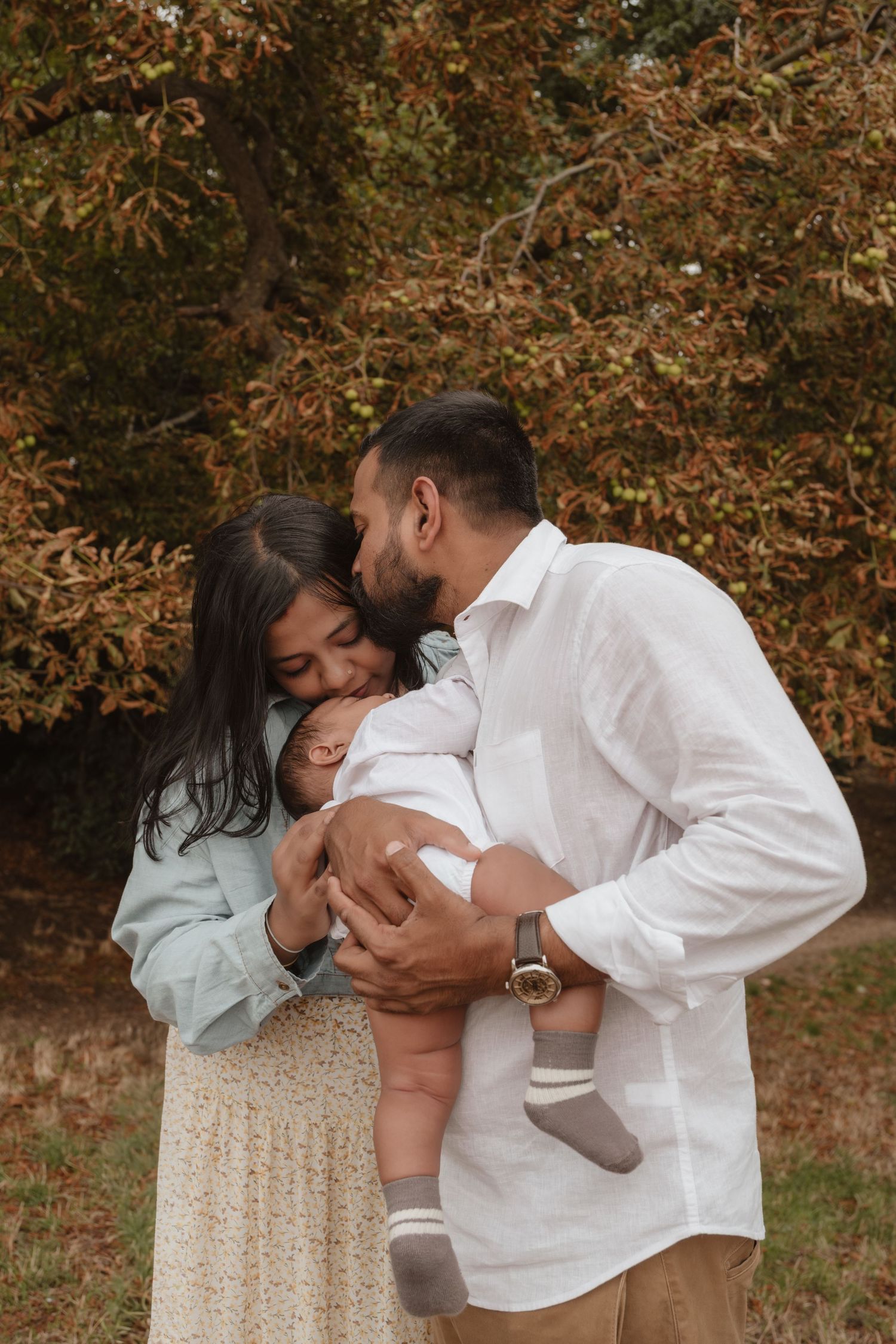 Family shares tender moments with their baby outdoors during autumn.