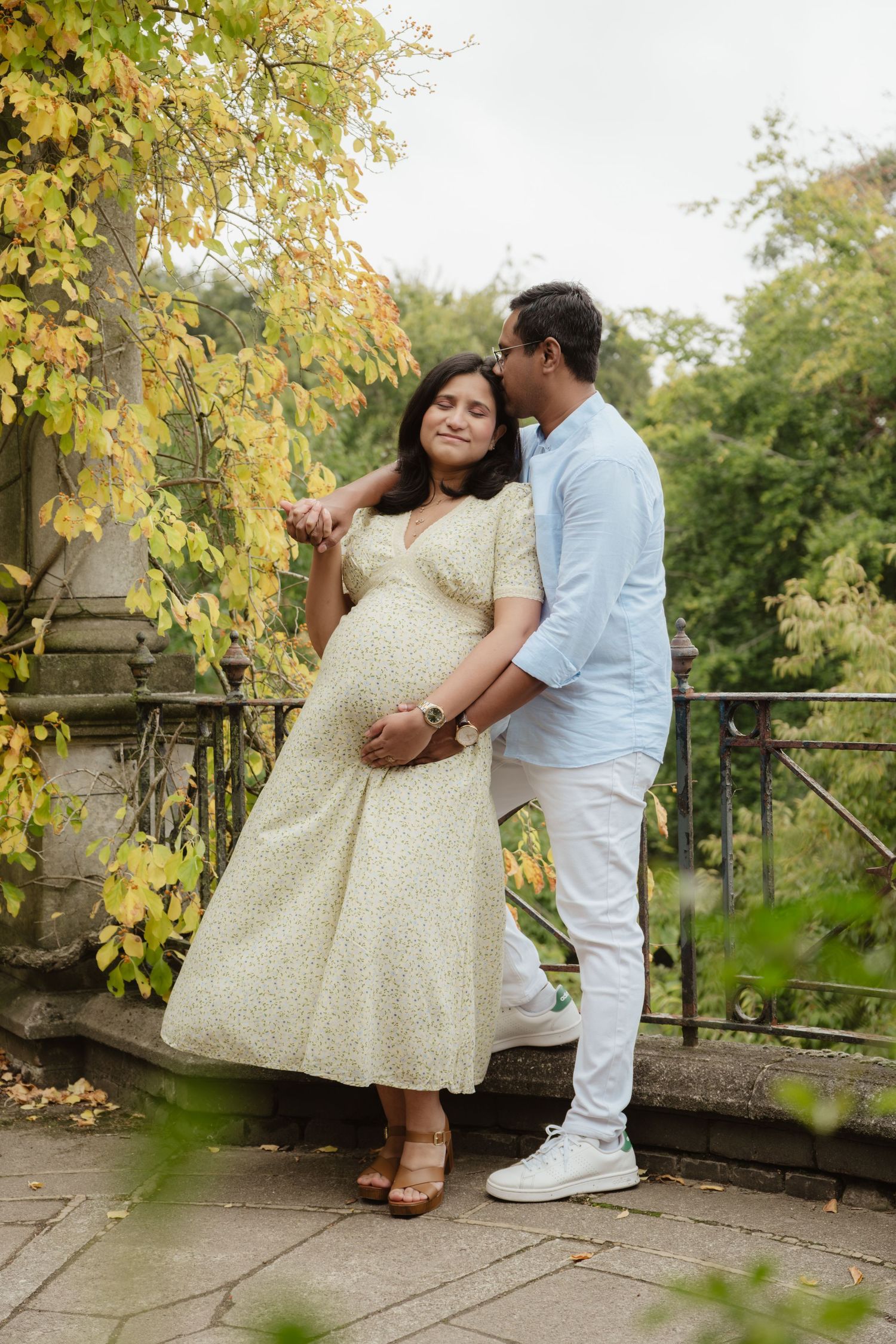 A romantic autumn maternity photoshoot on a stone terrace surrounded by yellow leaves.