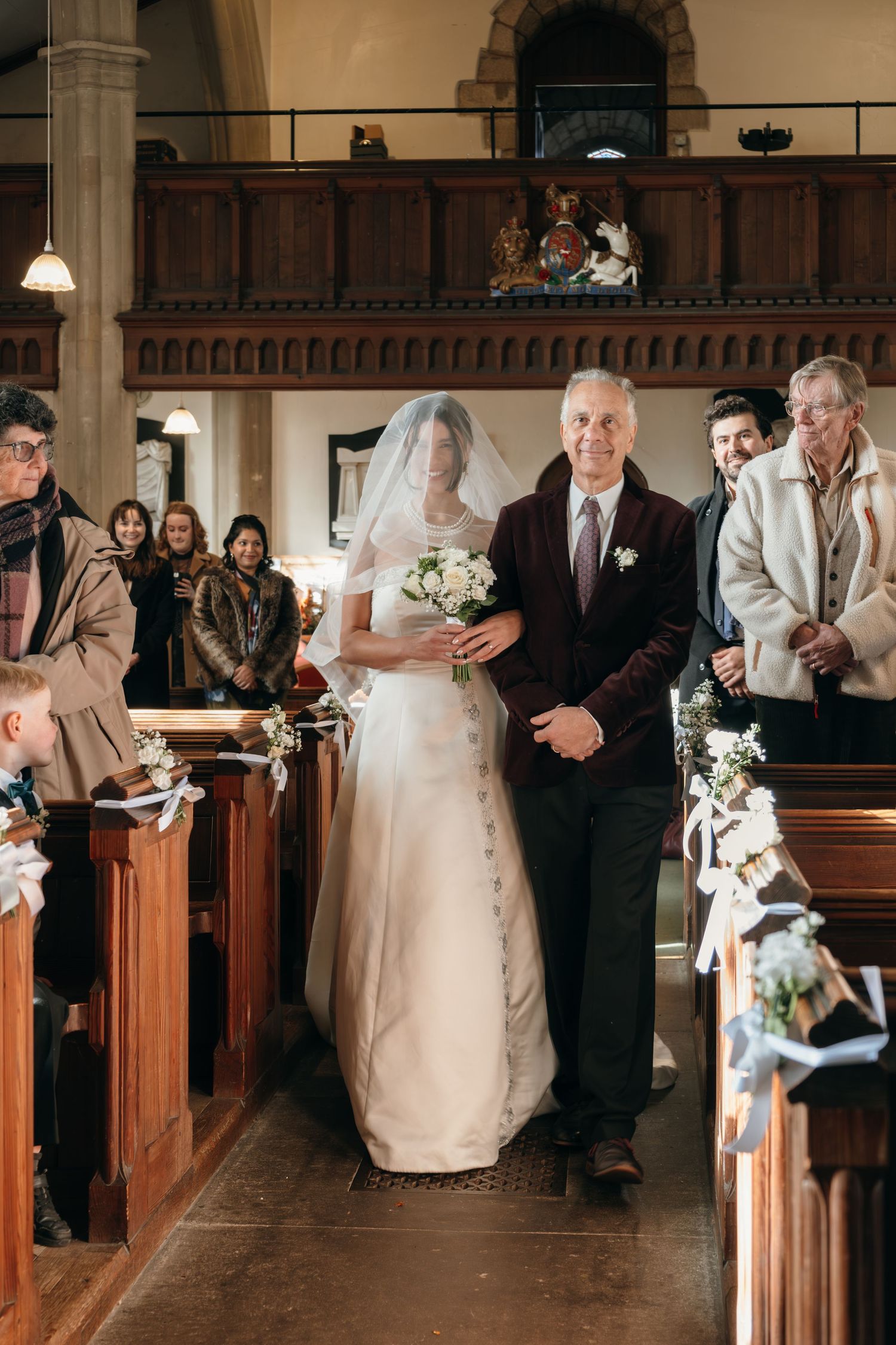 A traditional church wedding processional down the aisle with wooden pews and guests looking on.