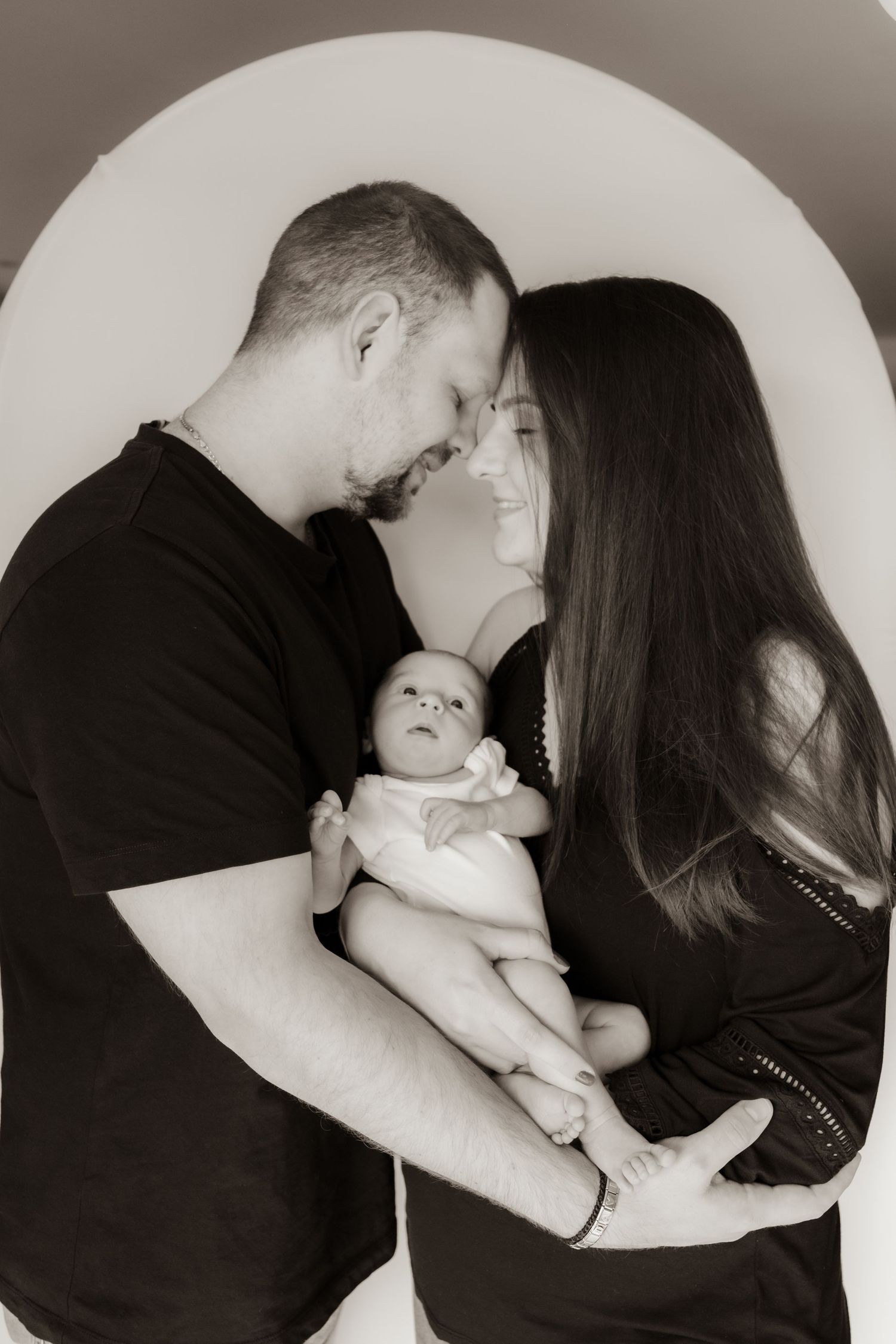 A series of black and white photographs showing tender moments between parents and a baby in intimate poses.