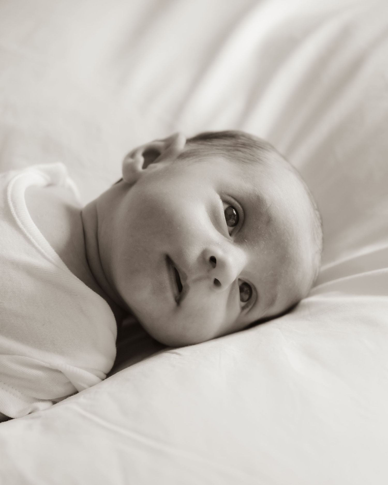 Black and white portrait series showing soft angles of resting figure against white sheets.