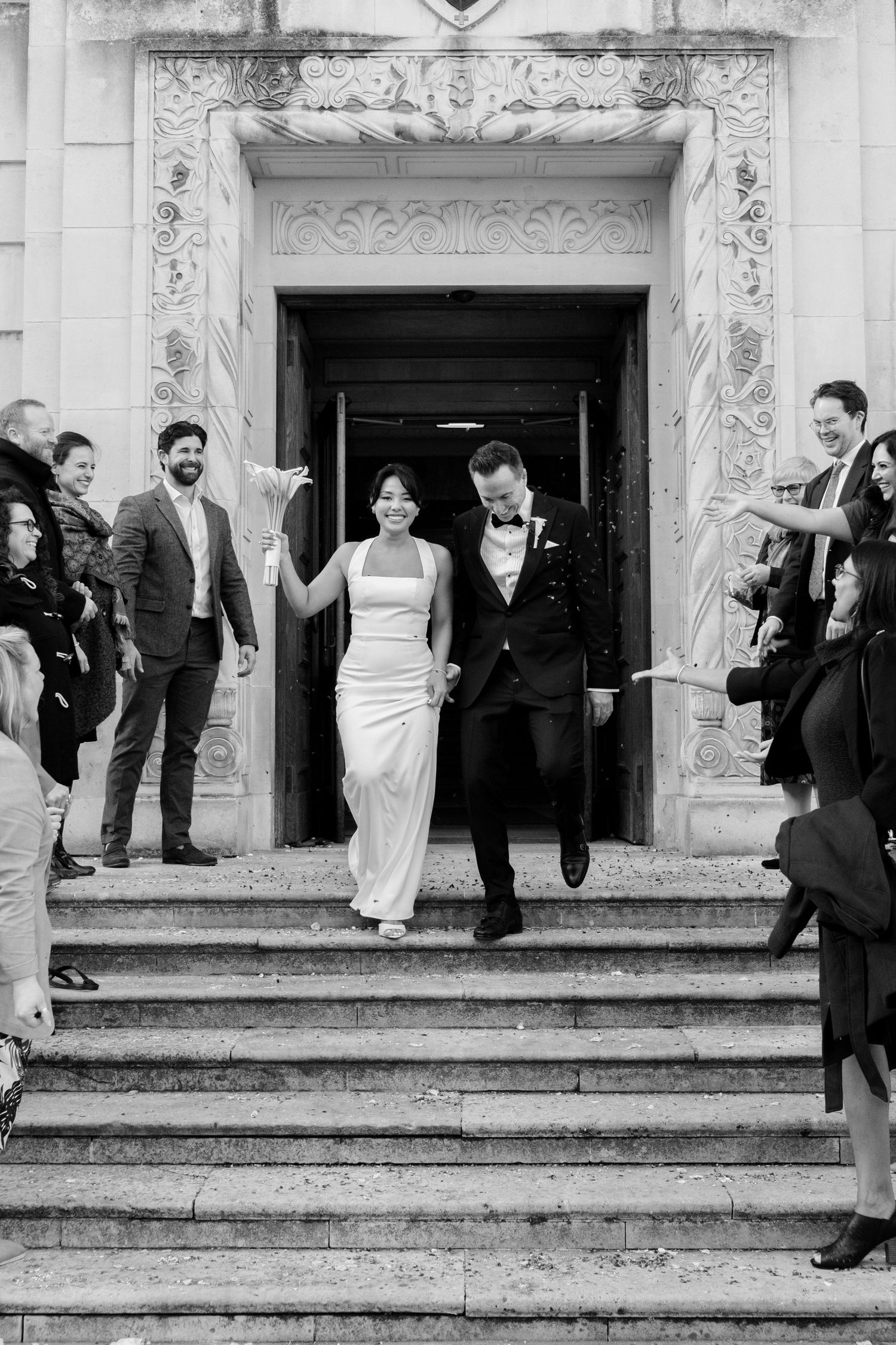 Wedding party exits church building with celebratory poses on stone steps.