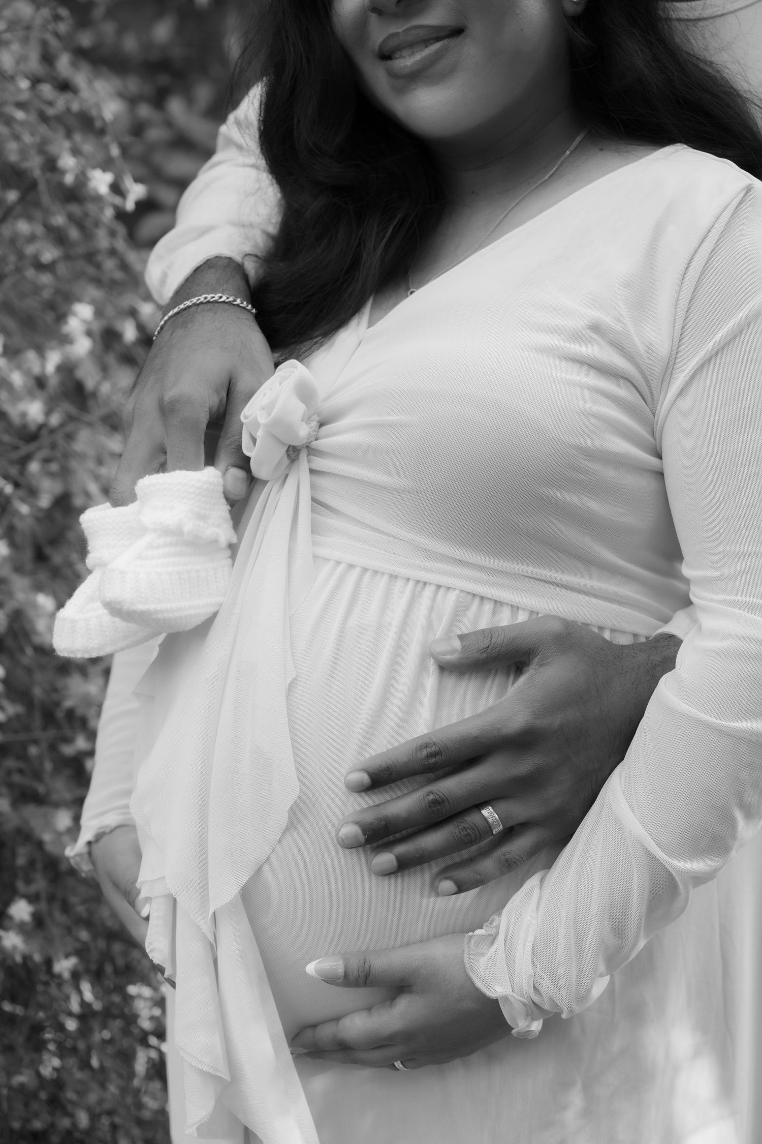 Close-up details of white maternity dress with hands cradling baby bump.