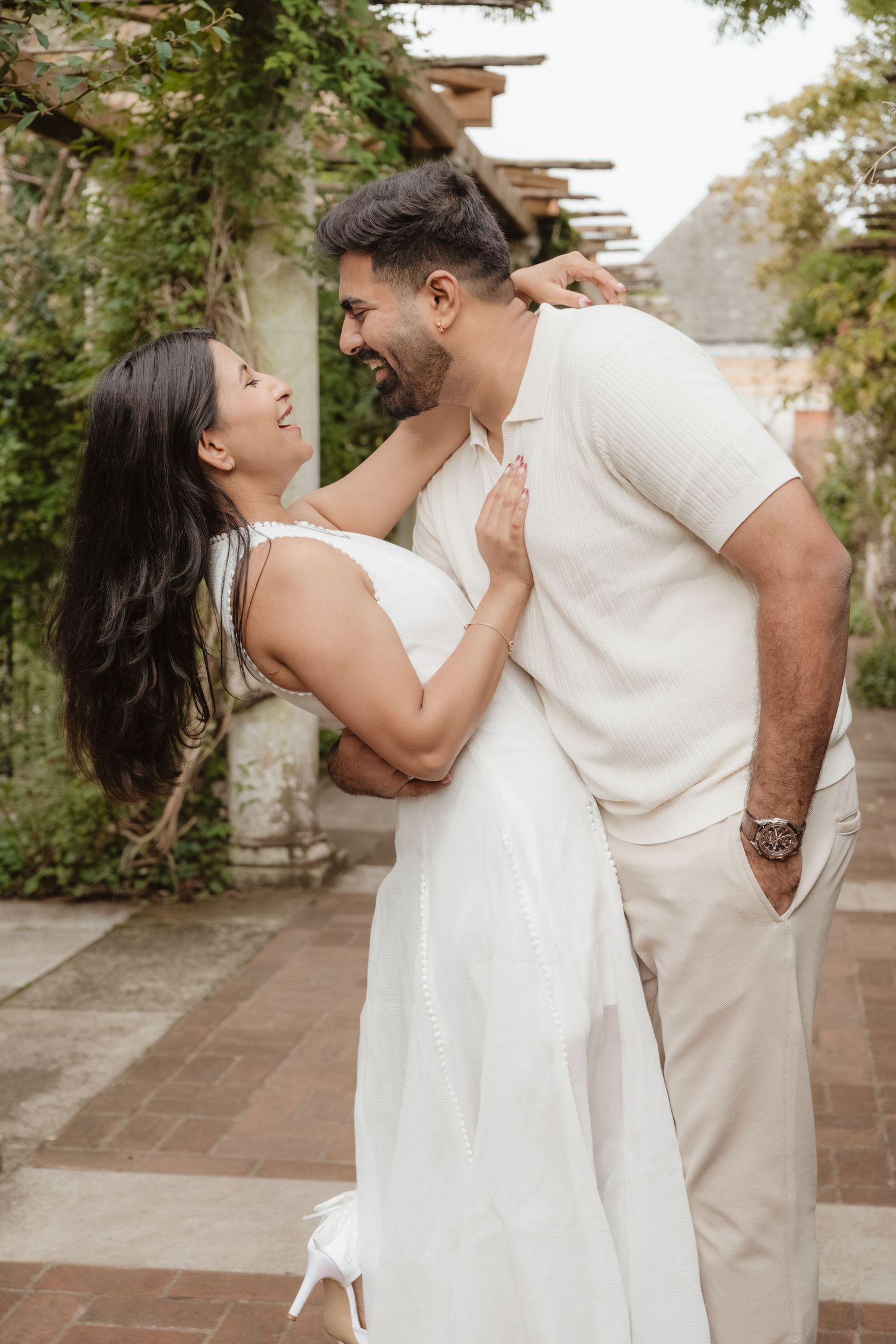A couple in matching white outfits dances together in a garden setting.