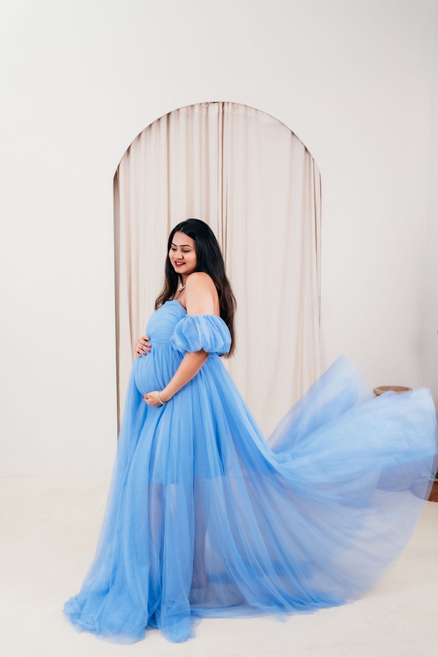 Maternity photoshoot featuring a flowing blue tulle gown against a light backdrop.