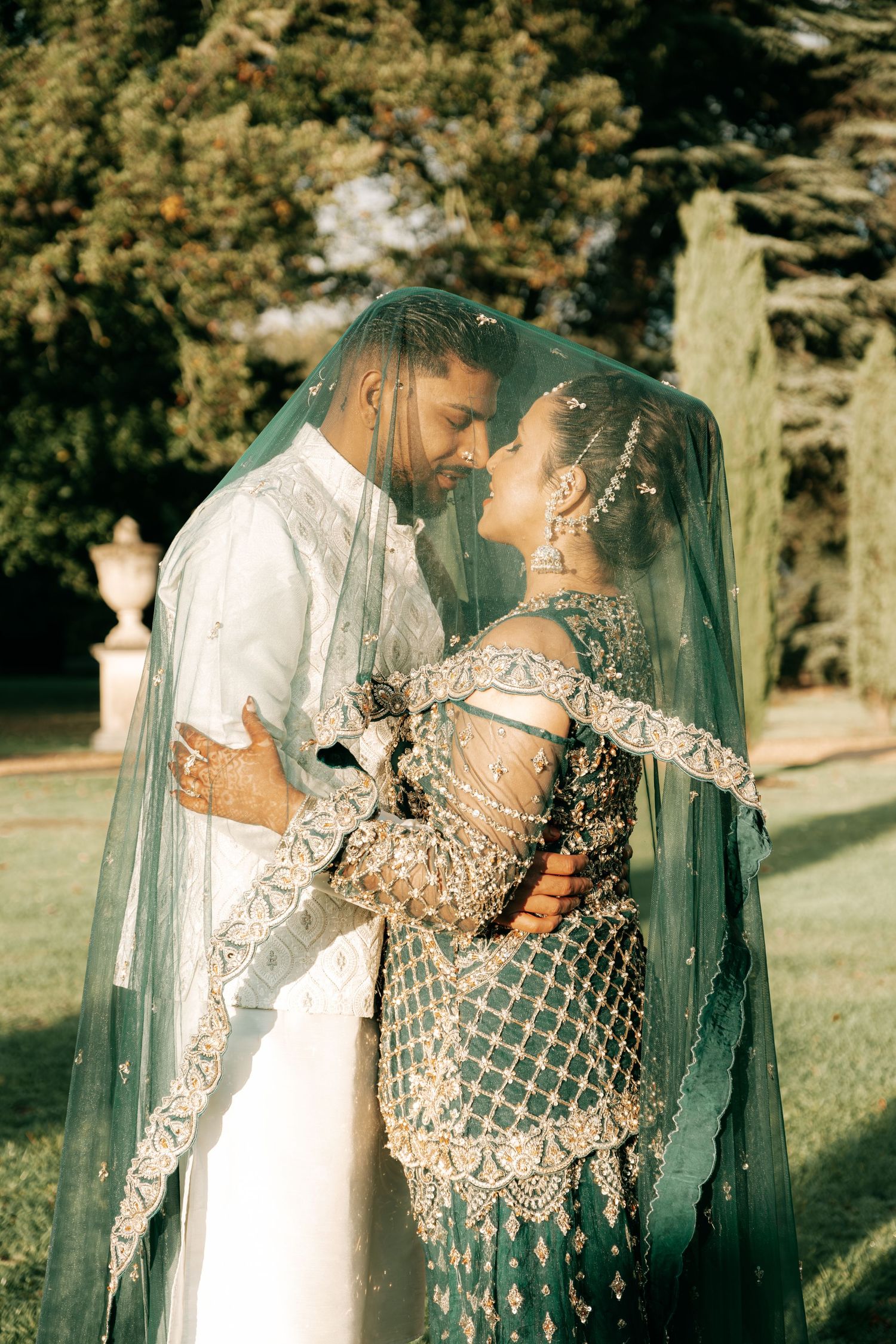 A romantic wedding portrait in a garden with the couple embracing under a flowing green veil.