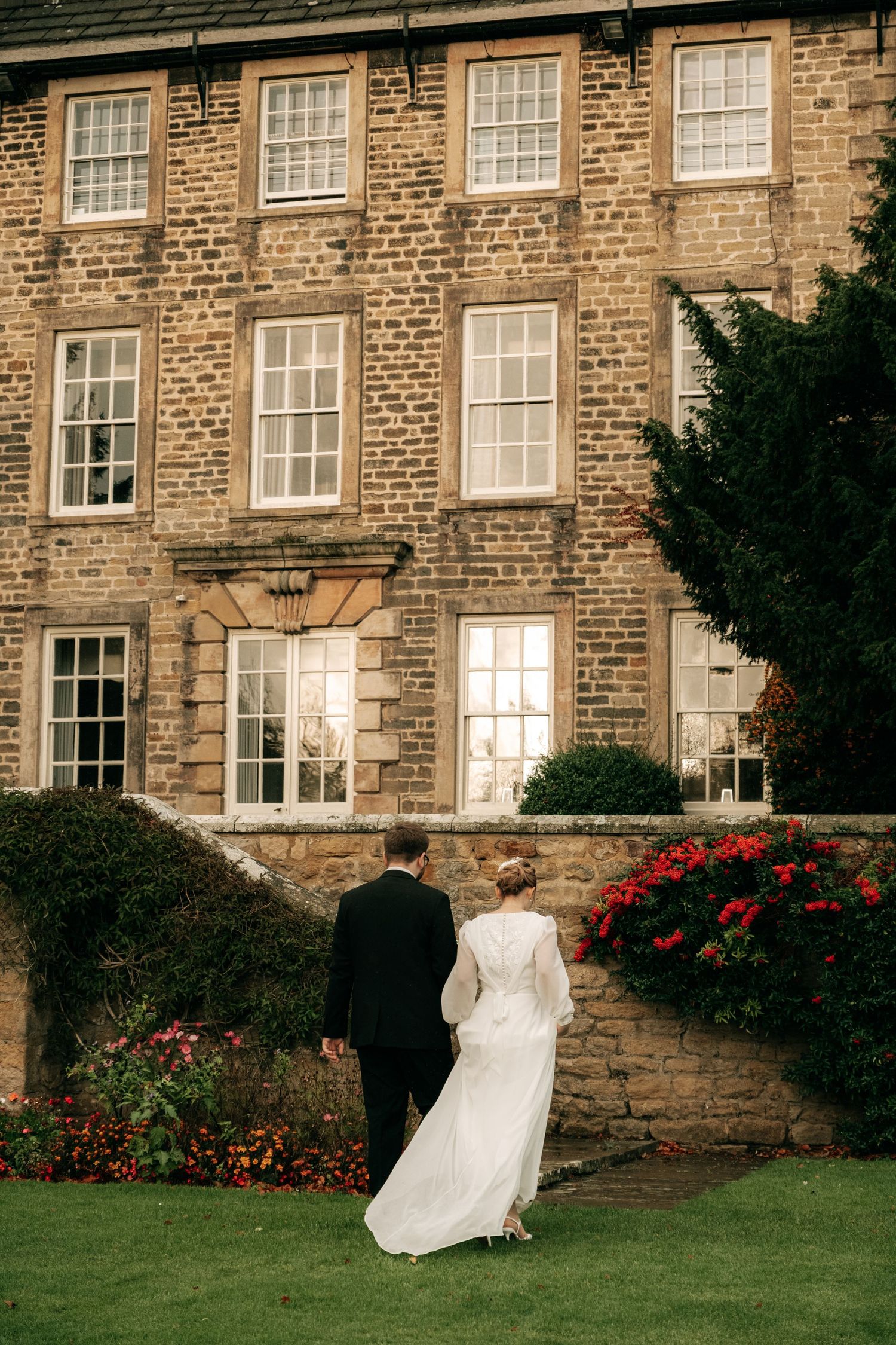 Wedding photos in front of a historic brick building with red flowers and green lawn.