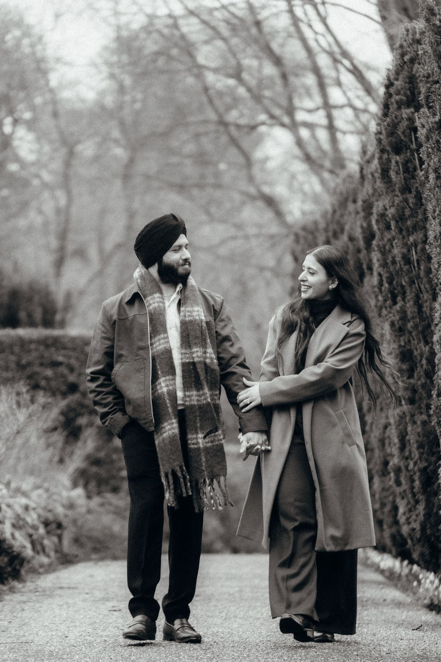 A couple shares a joyful moment while walking along a garden path in winter coats.