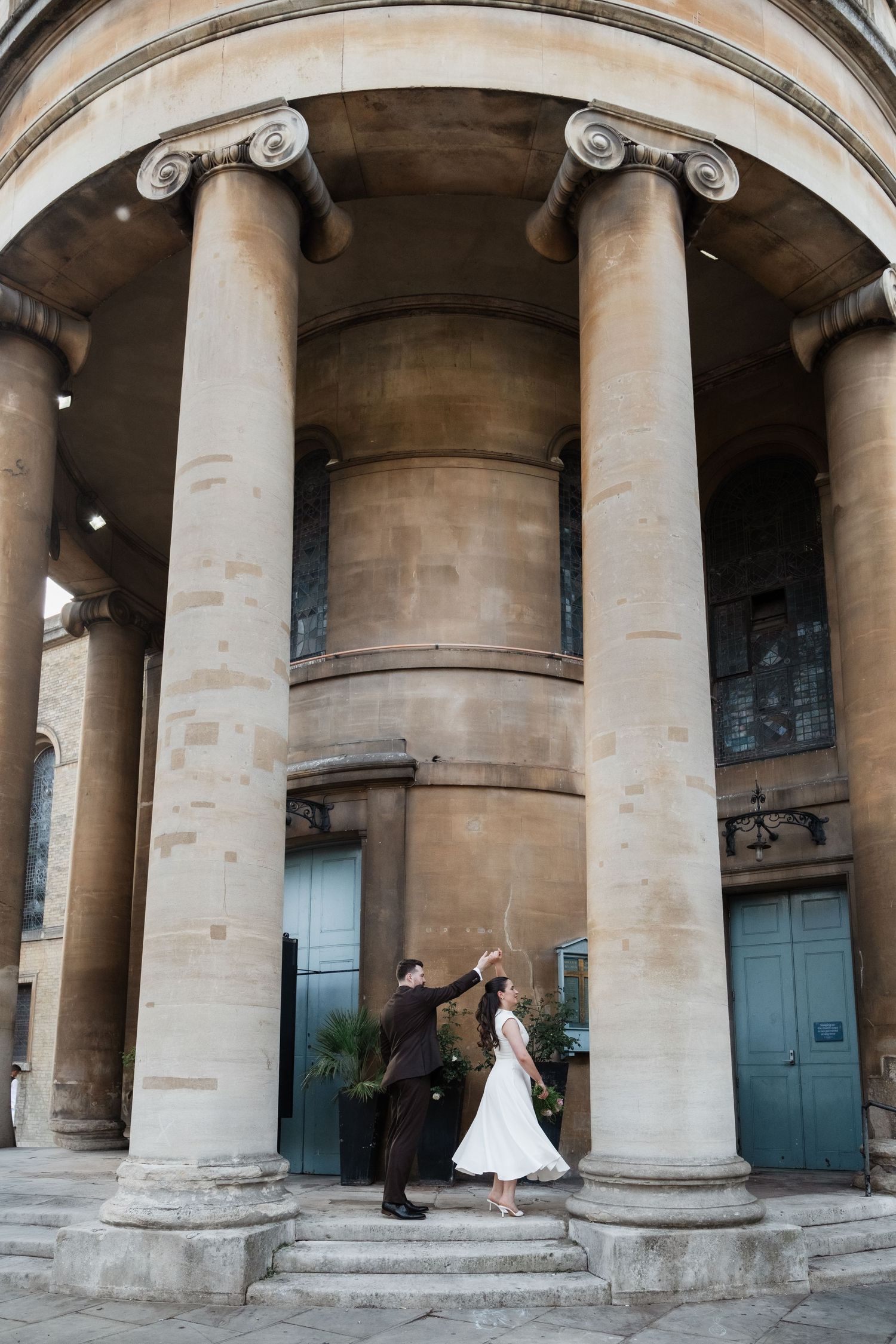 Couple dancing elegantly before grand neoclassical columns at a historic stone building during wedding celebration.