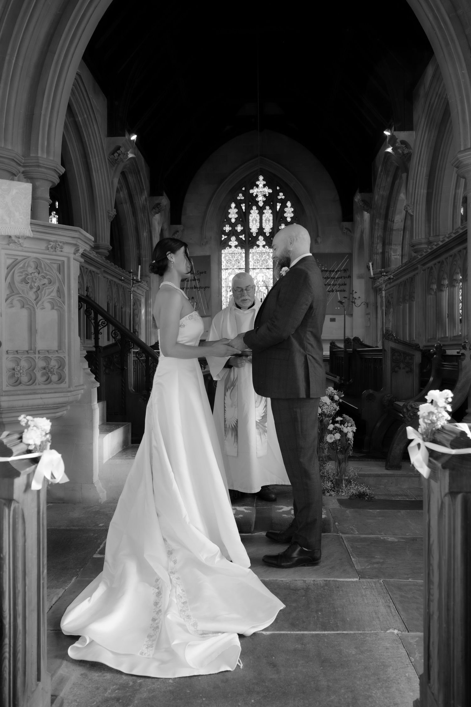 A black and white photograph of a wedding ceremony inside a gothic church with arched windows.