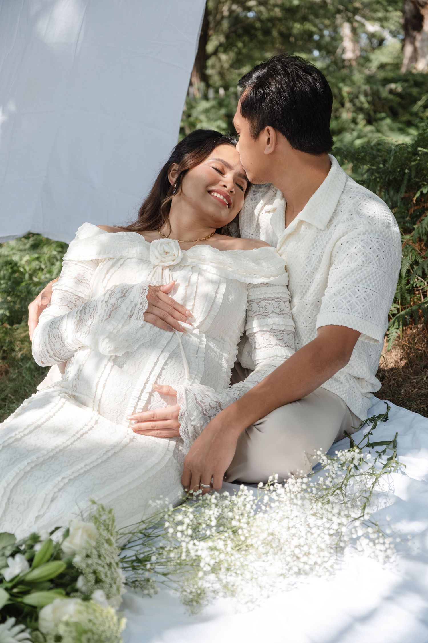 Romantic maternity photos with white lace dresses and baby's breath flowers in garden setting.