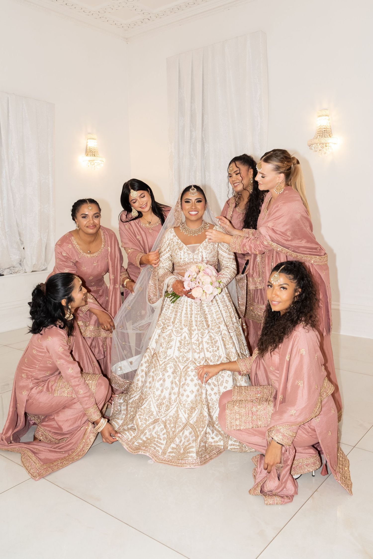 Wedding party in pink dresses gathered around bride in ornate gold gown.