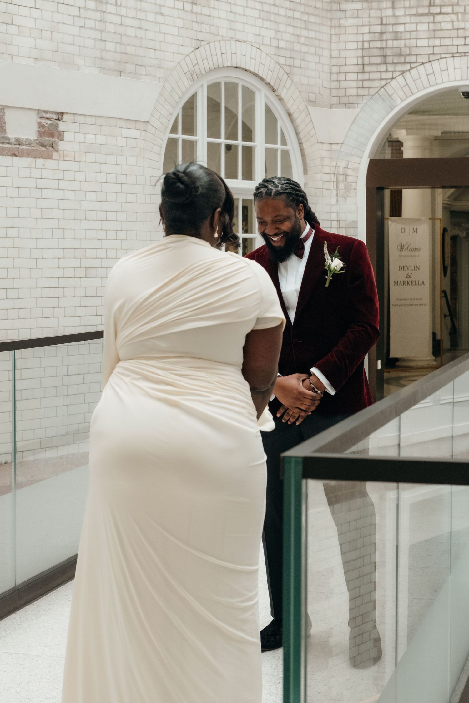 A couple shares a tender moment in an elegant white brick hallway.
