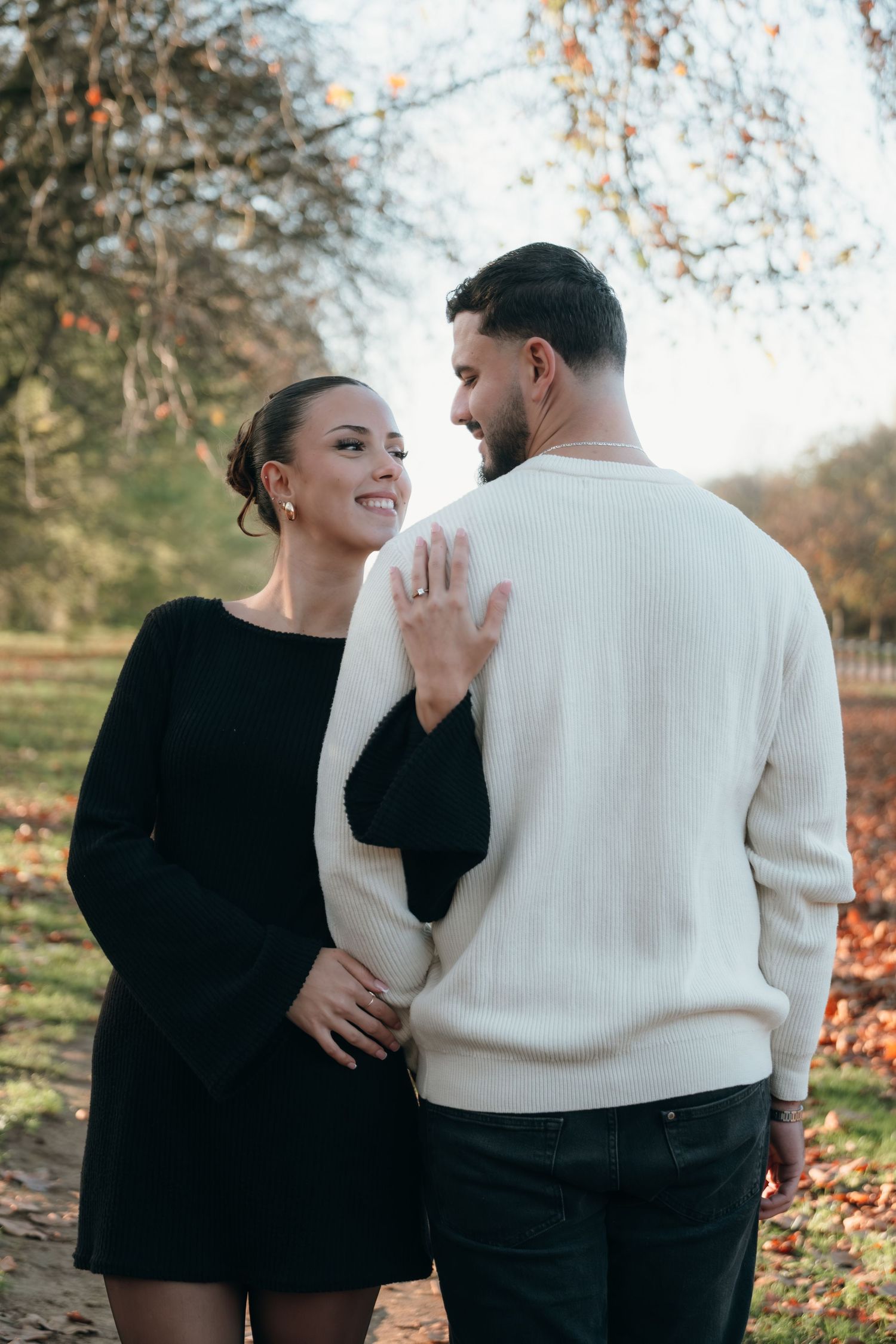 A couple shares a joyful moment outdoors during autumn with fallen leaves in the background.