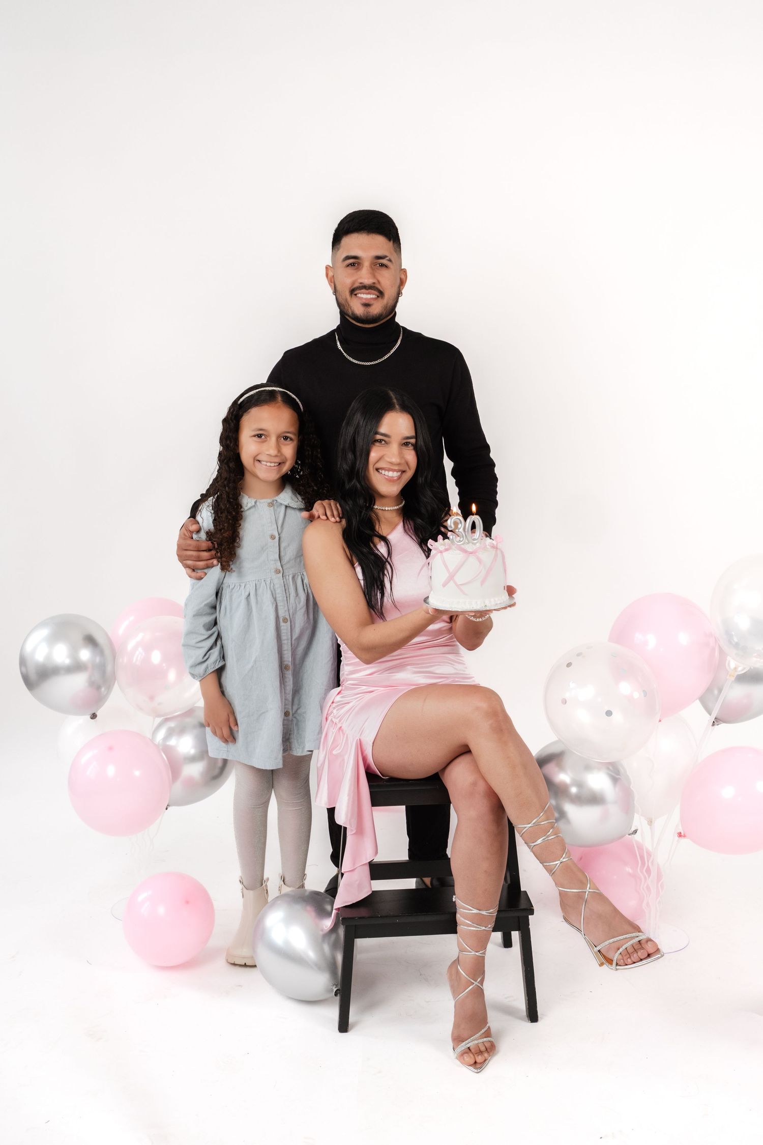 Studio family photoshoot with pink and silver balloons against white backdrop.
