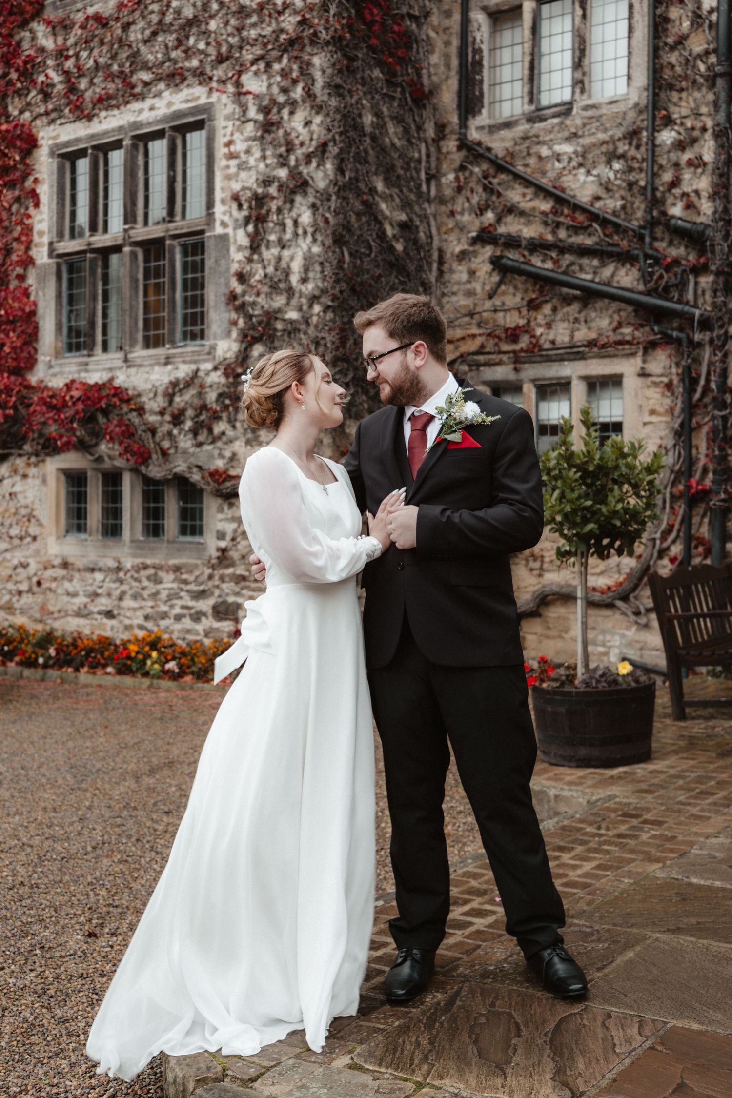 Romantic wedding portrait against ivy-covered stone building in autumn.
