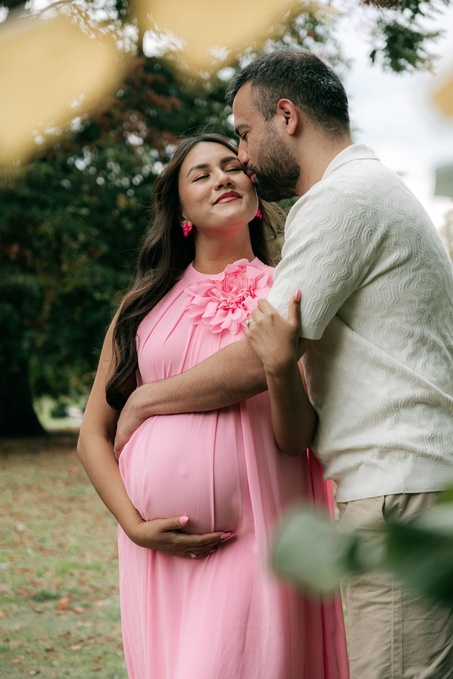 A couple shares an intimate moment outdoors while wearing pink and beige attire.