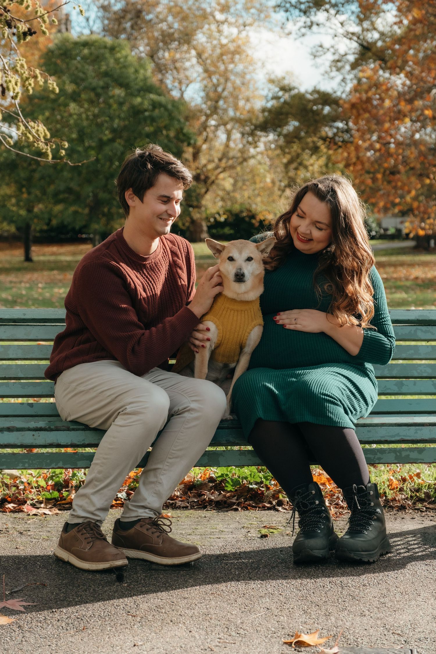 Couple sitting on park bench with their dog during autumn maternity session.