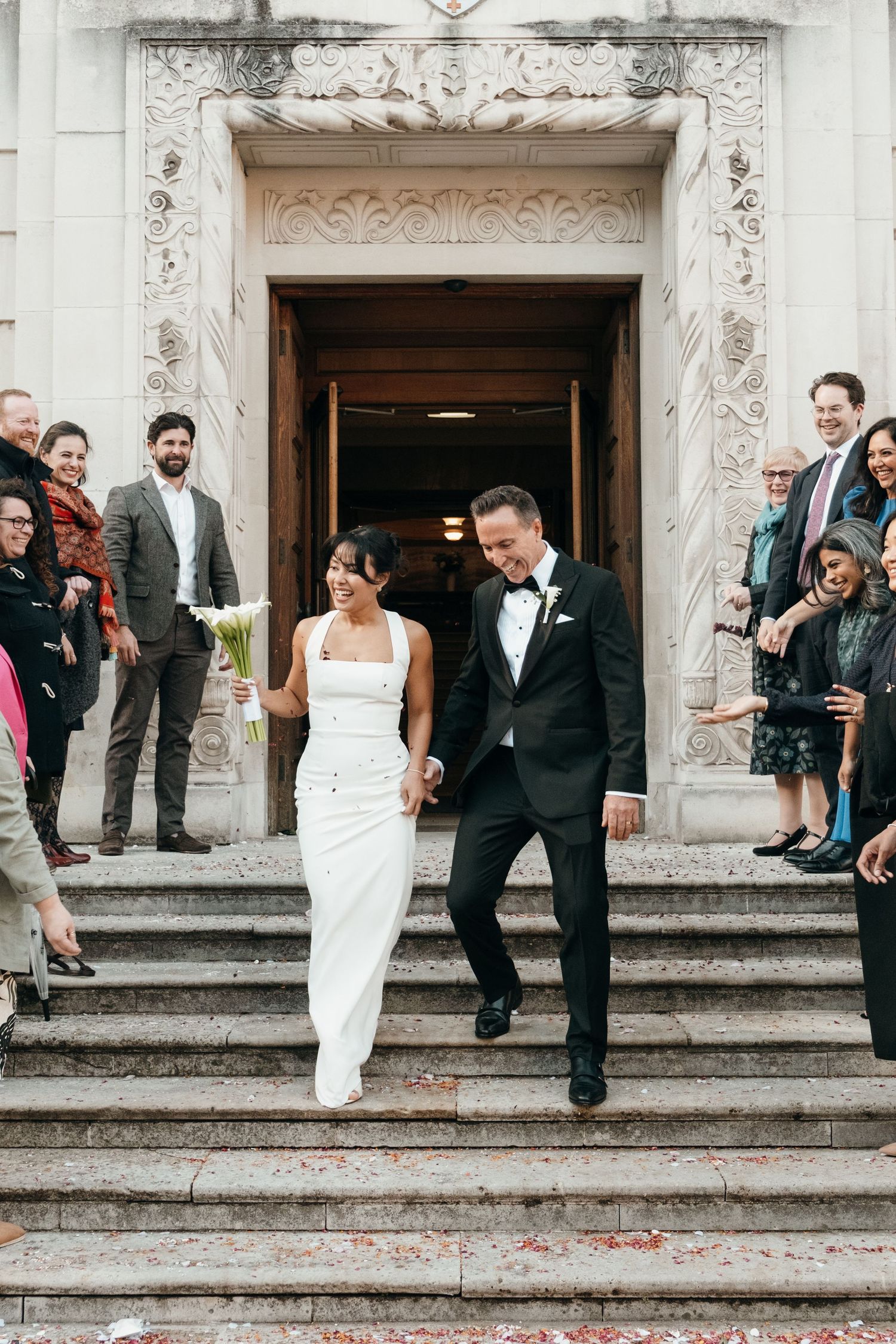Wedding couple descending ornate stone steps while guests look on from the sides.