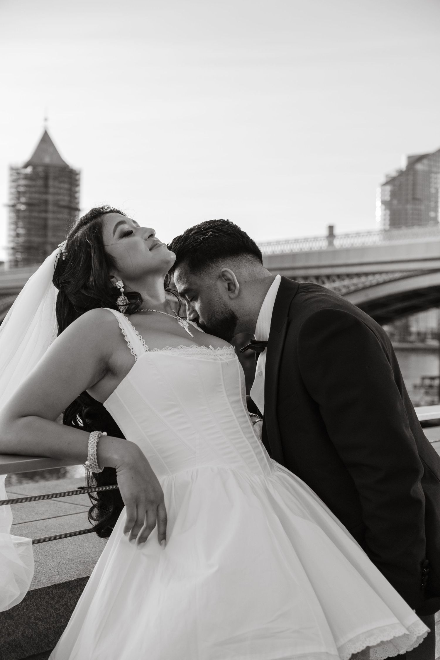 A dramatic black and white wedding photo of a couple posing on an urban bridge.