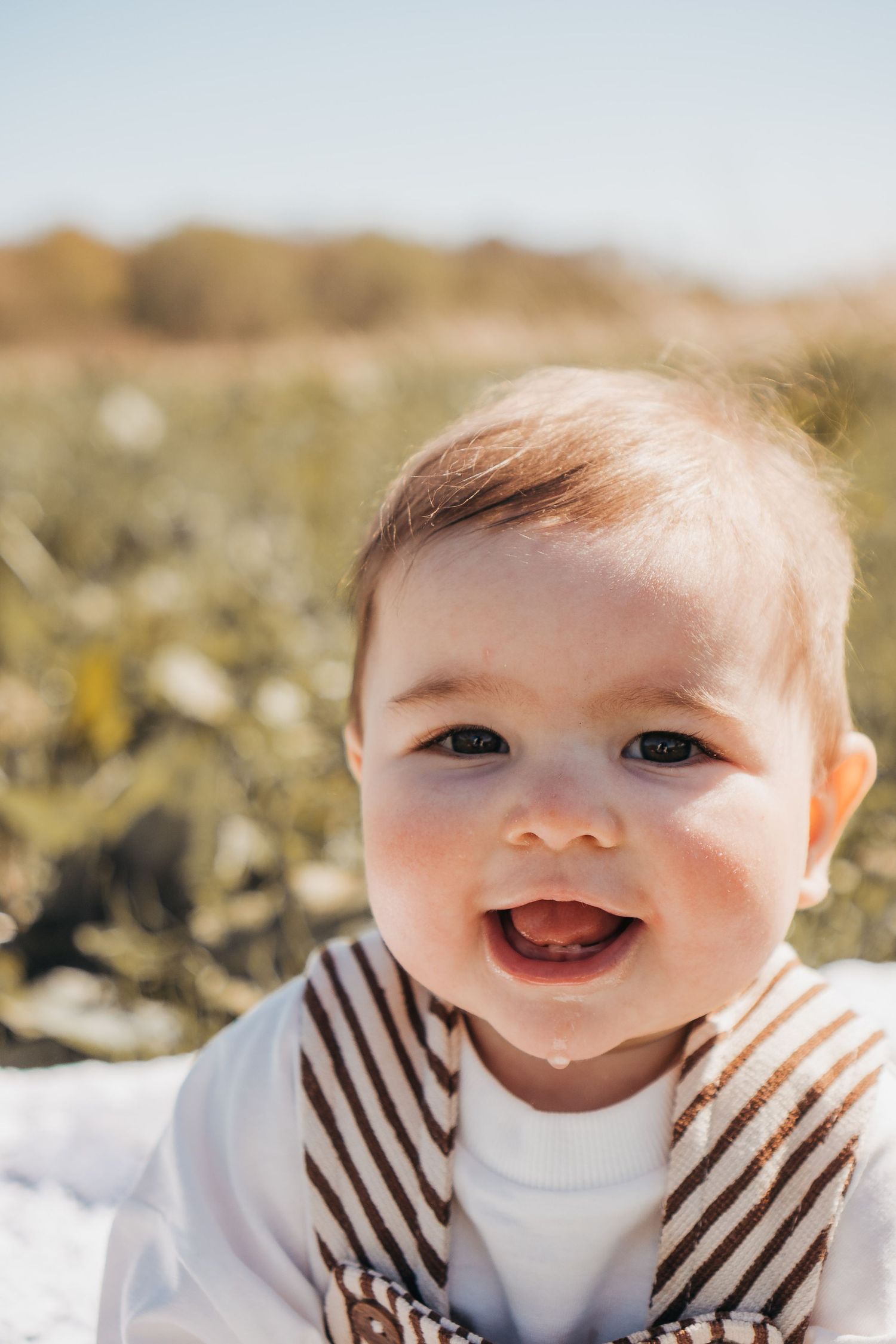 Smiling baby in a sunny field with green foliage background during a 6 month milestone