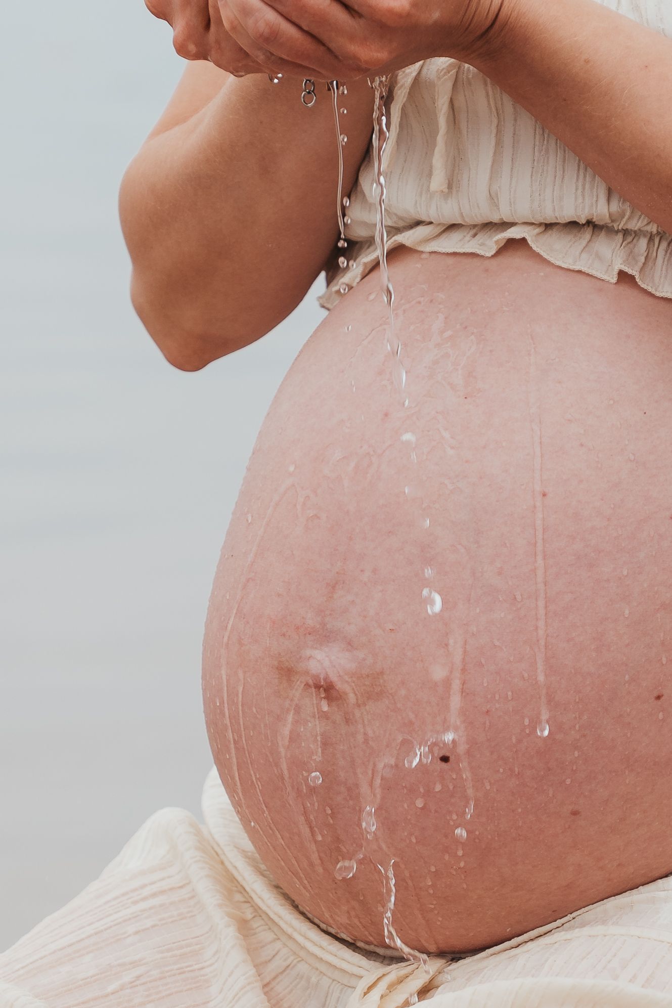 Close-up of pregnant belly with water droplets dripping down bare bump outdoors.