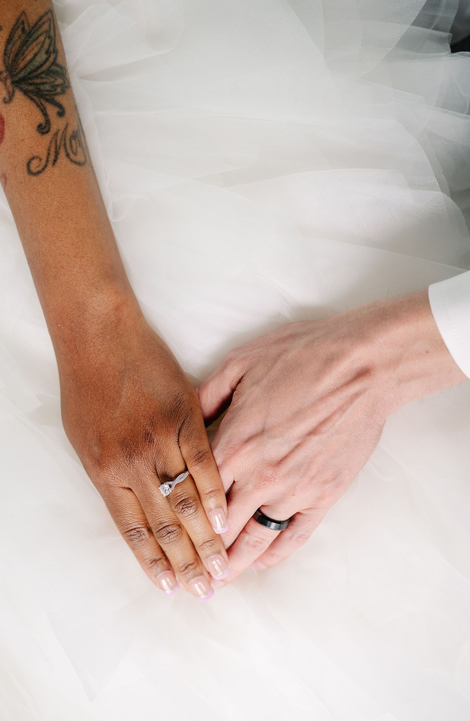 Close-up of hands wearing wedding rings resting on white tulle fabric.