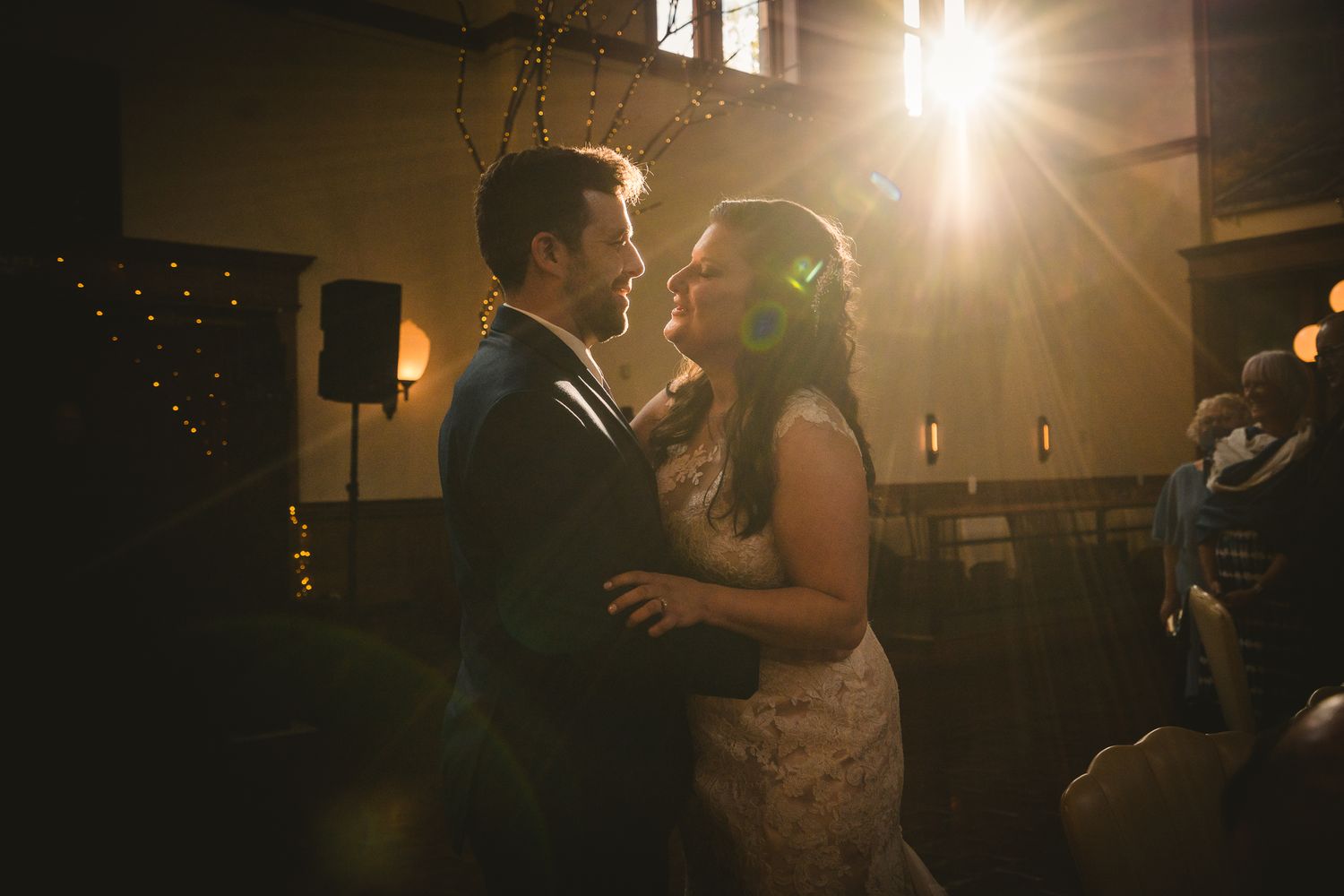 A couple shares their first dance at a wedding reception under warm lighting of sunset.