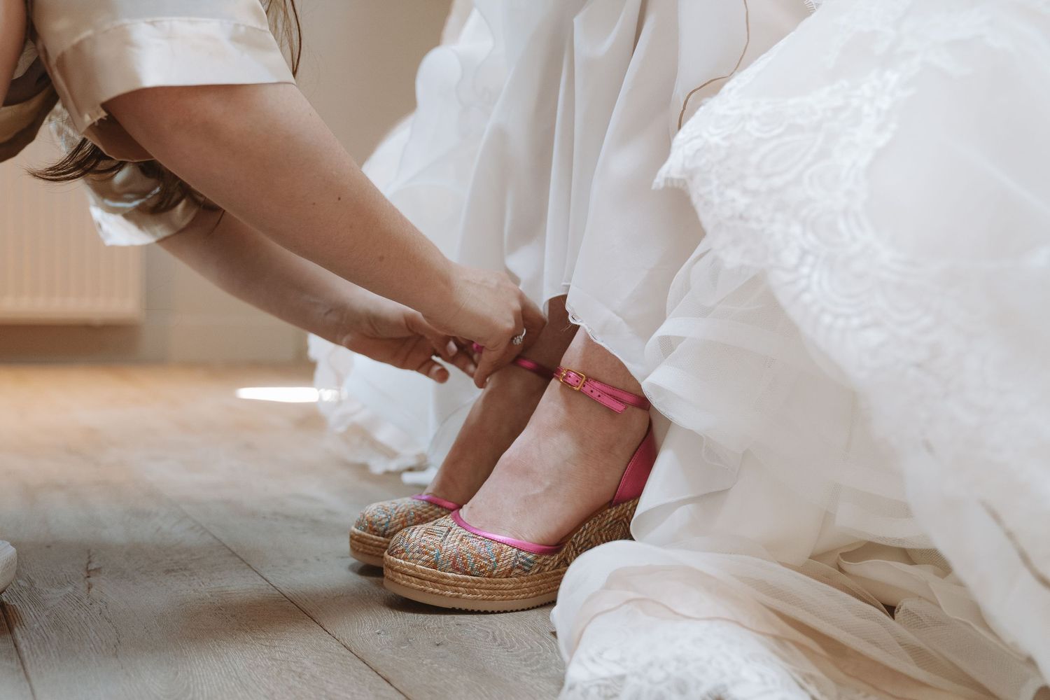 Close-up van bruidsschoenen en trouwjurk op houten vloer, bridesmaid helpt haar – bruidsfotografie, bridal details, trouwdag