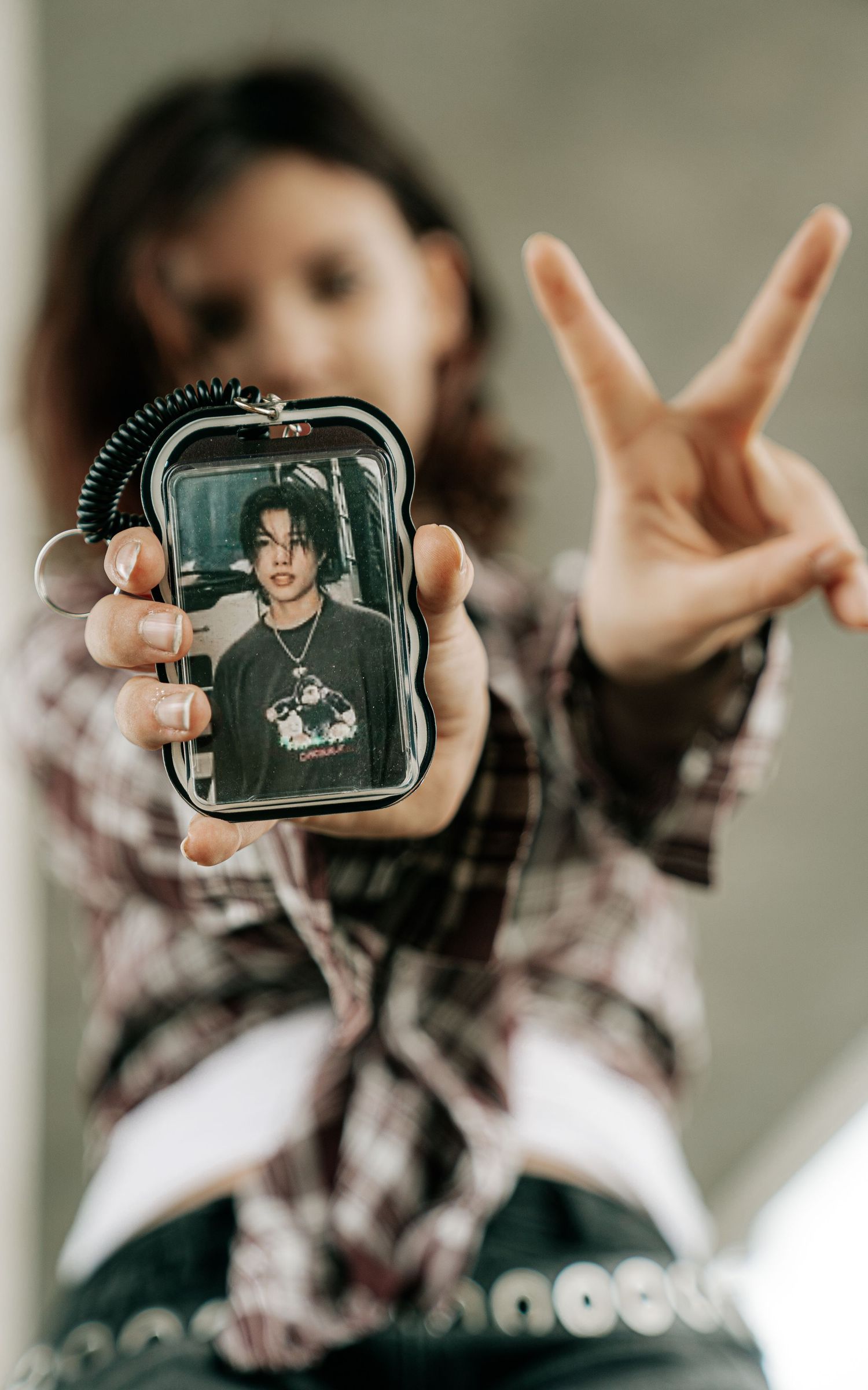Person holding a photo keychain while making a peace sign, wearing a plaid shirt.
