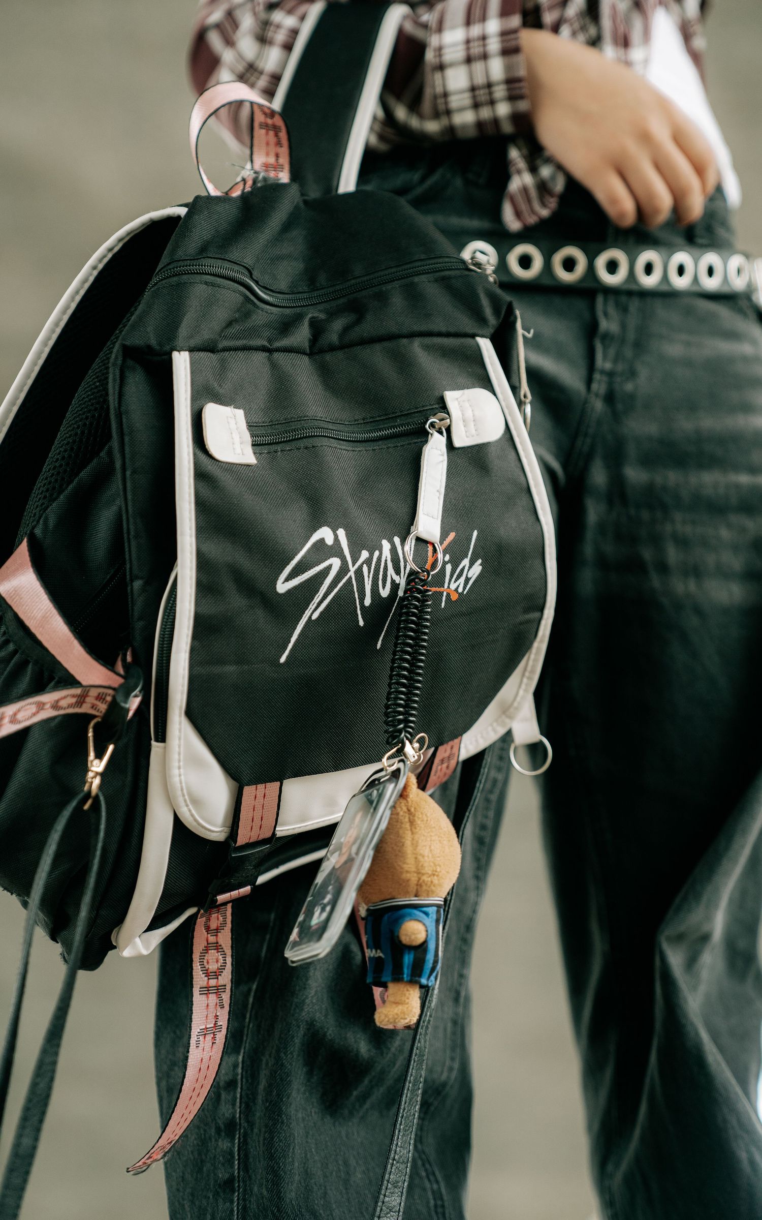 Black Stray Kids branded backpack with keychains, worn with plaid shirt and jeans.