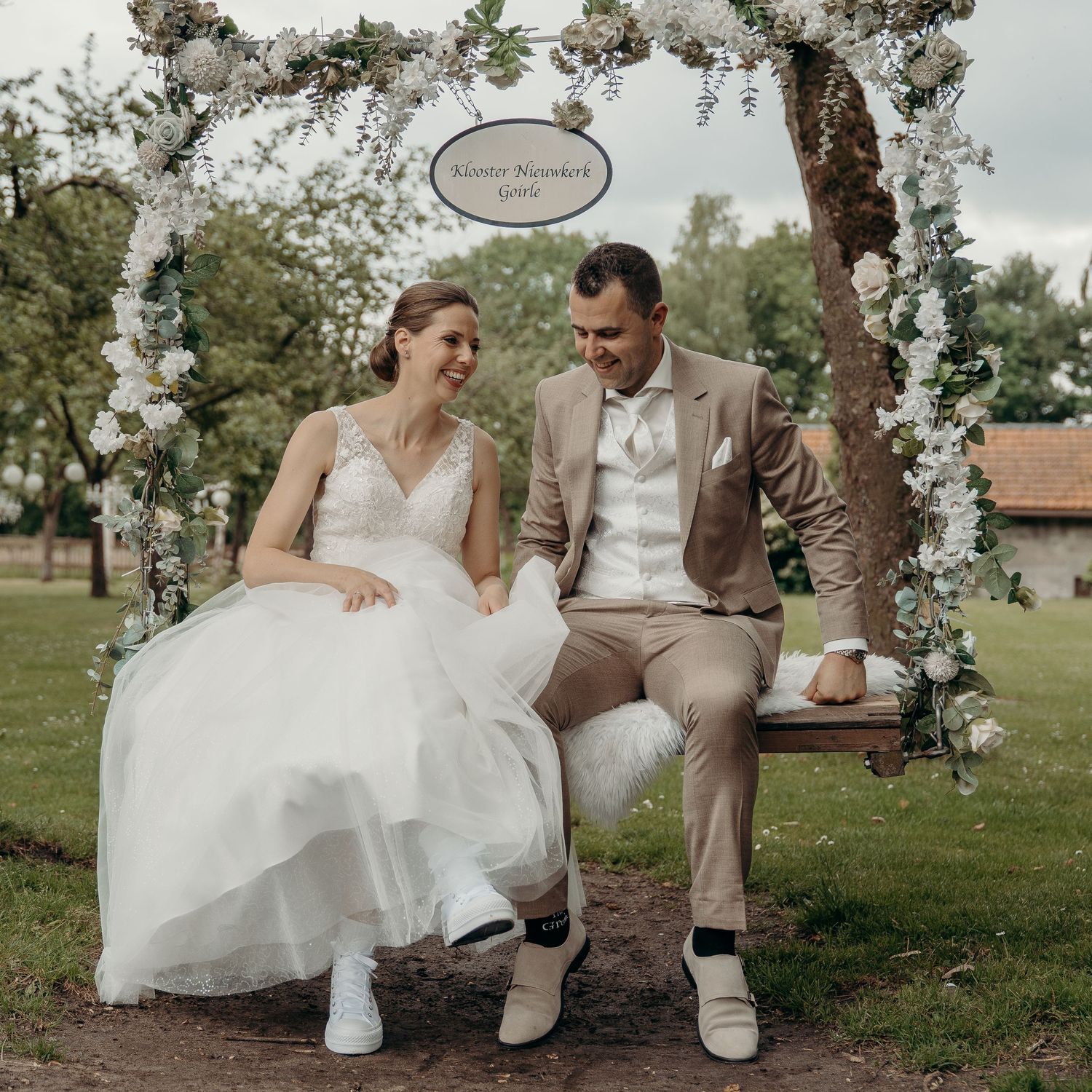 Romantische trouwportretten onder bloemenboog in buitenlocatie Klooster Nieuwkerk, Goirle – bruidsfotografie, trouwdag, Nederland
