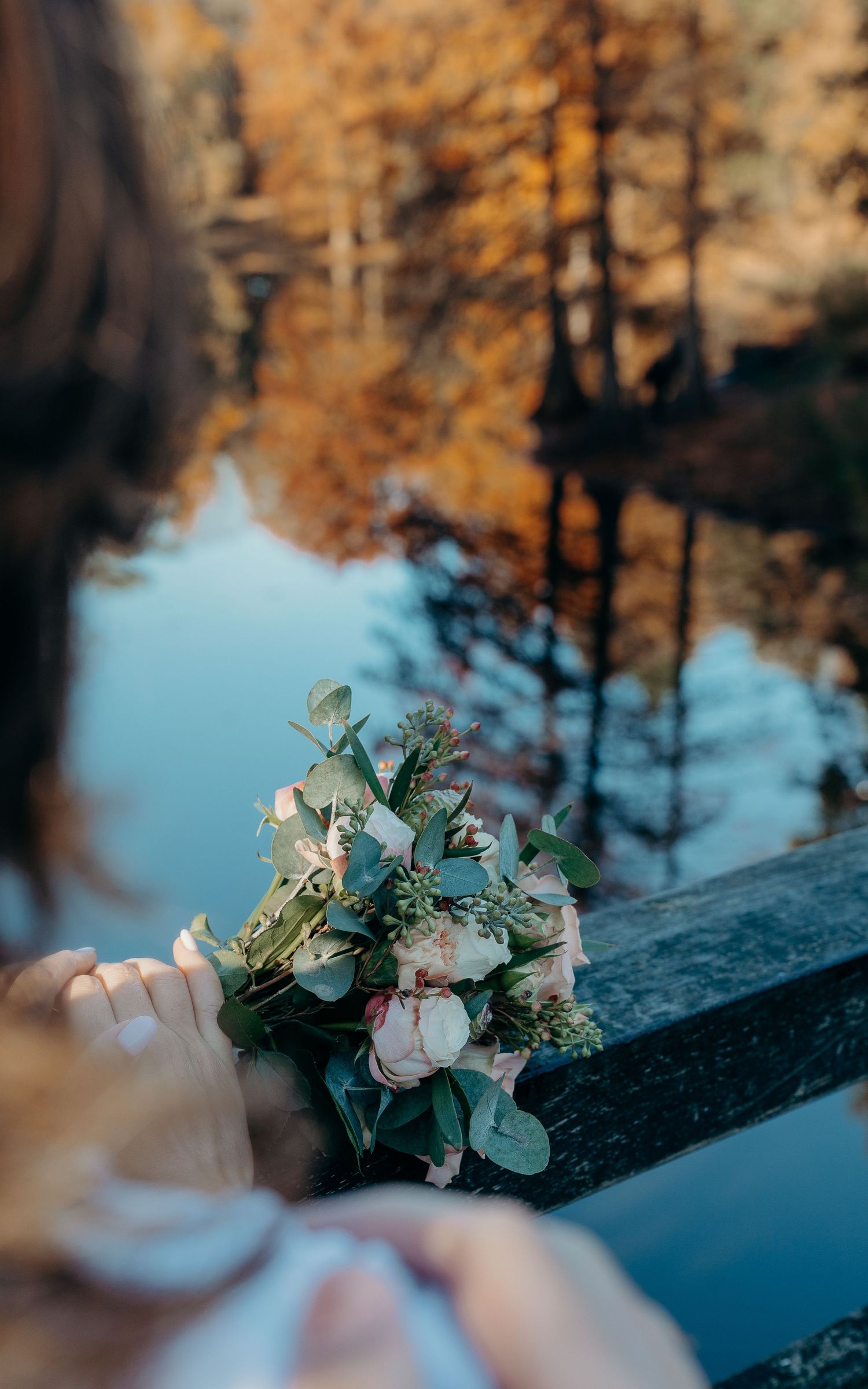 Bruidsboeket op brug in Wandelbos Tilburg met herfstbladeren weerspiegeld – bruidsfotografie, bridal details, Nederland