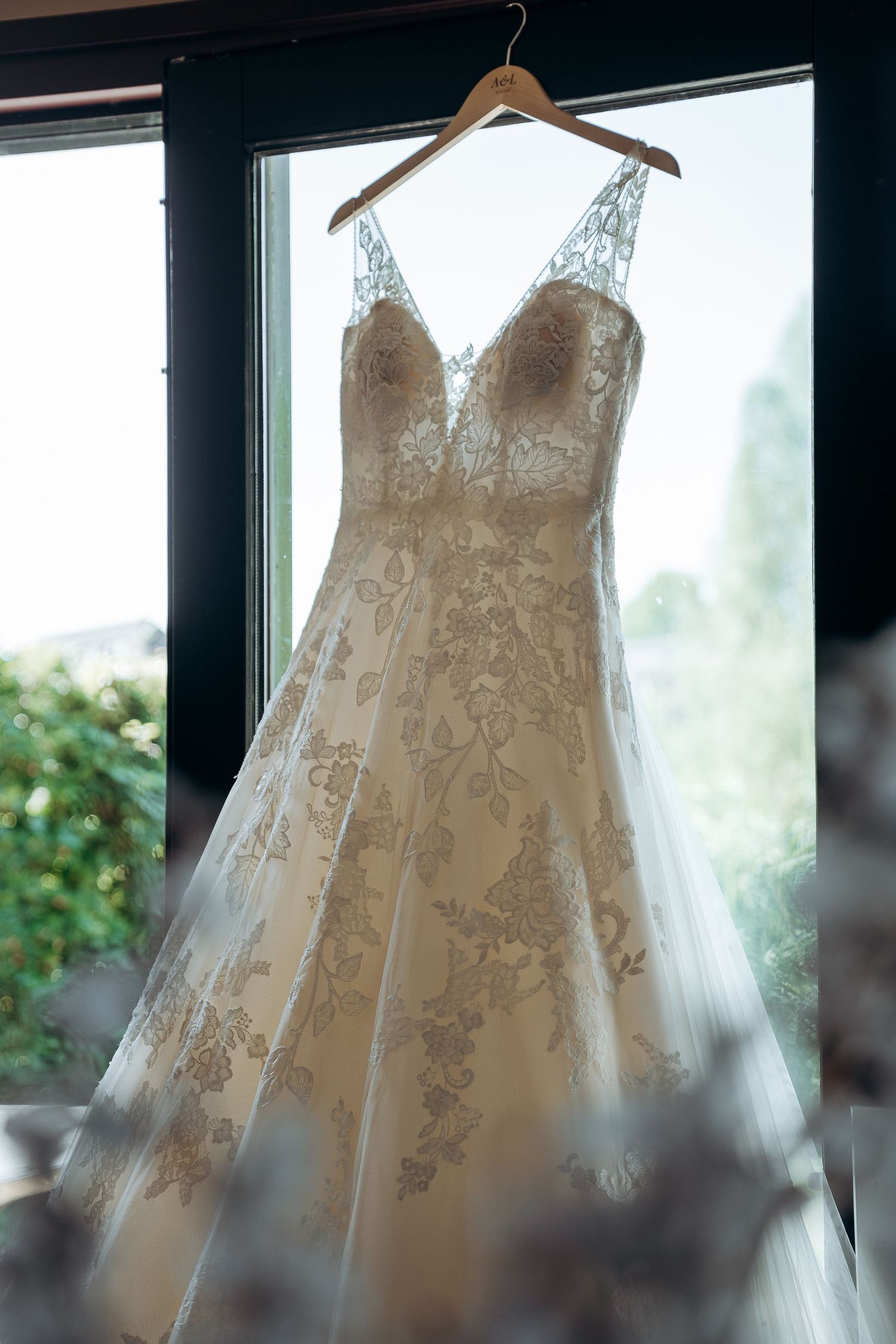 Trouwjurk met delicaat kanten details hangend in natuurlijk raamlicht – bruidsfotografie, bridal details, trouwdag, Nederland
