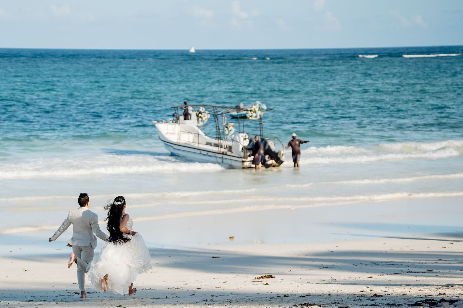 Couple running towards boat on tropical beach with turquoise waters.