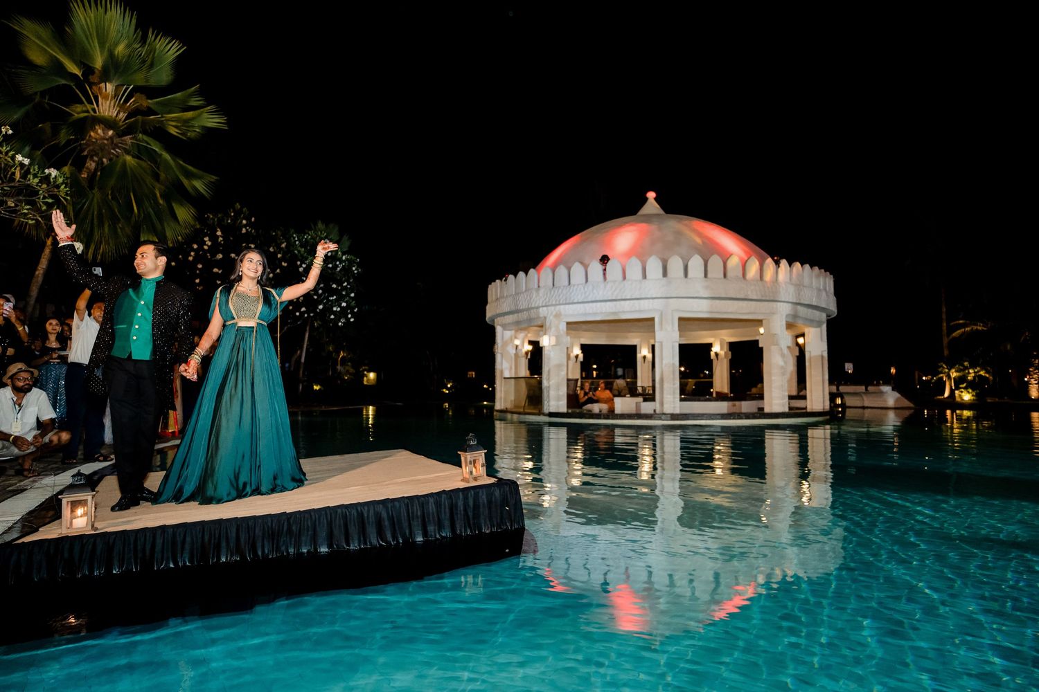 Couple poses in evening attire near an illuminated gazebo and pool.