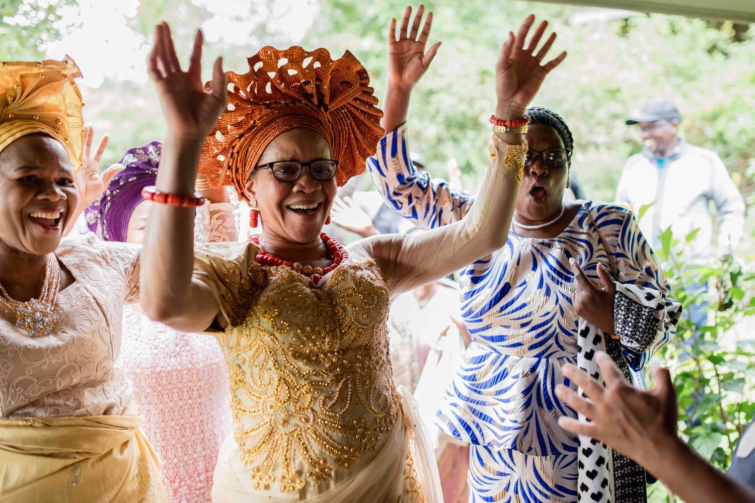 Festive celebration scene with guests wearing colorful attire dancing with raised hands.