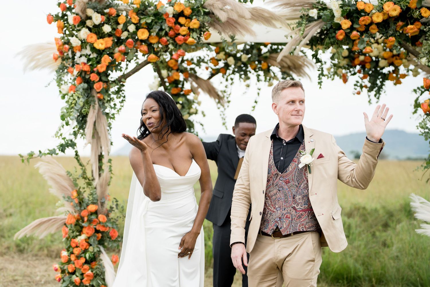 Newlyweds celebrating under orange floral arch after outdoor ceremony.