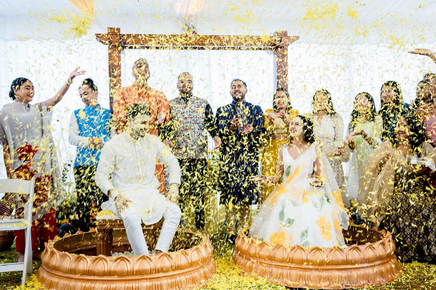 Festive outdoor wedding ceremony with flower petals raining down on a decorated mandap setup.