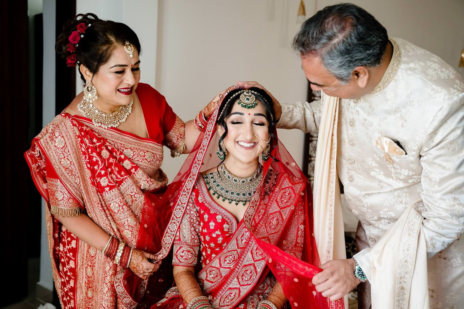 A joyful moment during traditional Indian wedding preparations with family members in red and white attire.