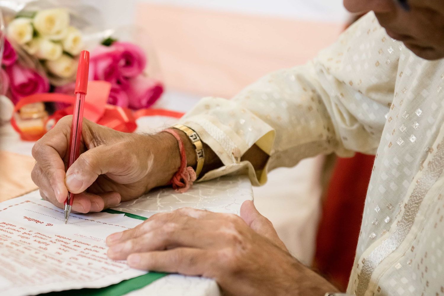Close up of hands signing wedding documents with roses and decorations in frame.