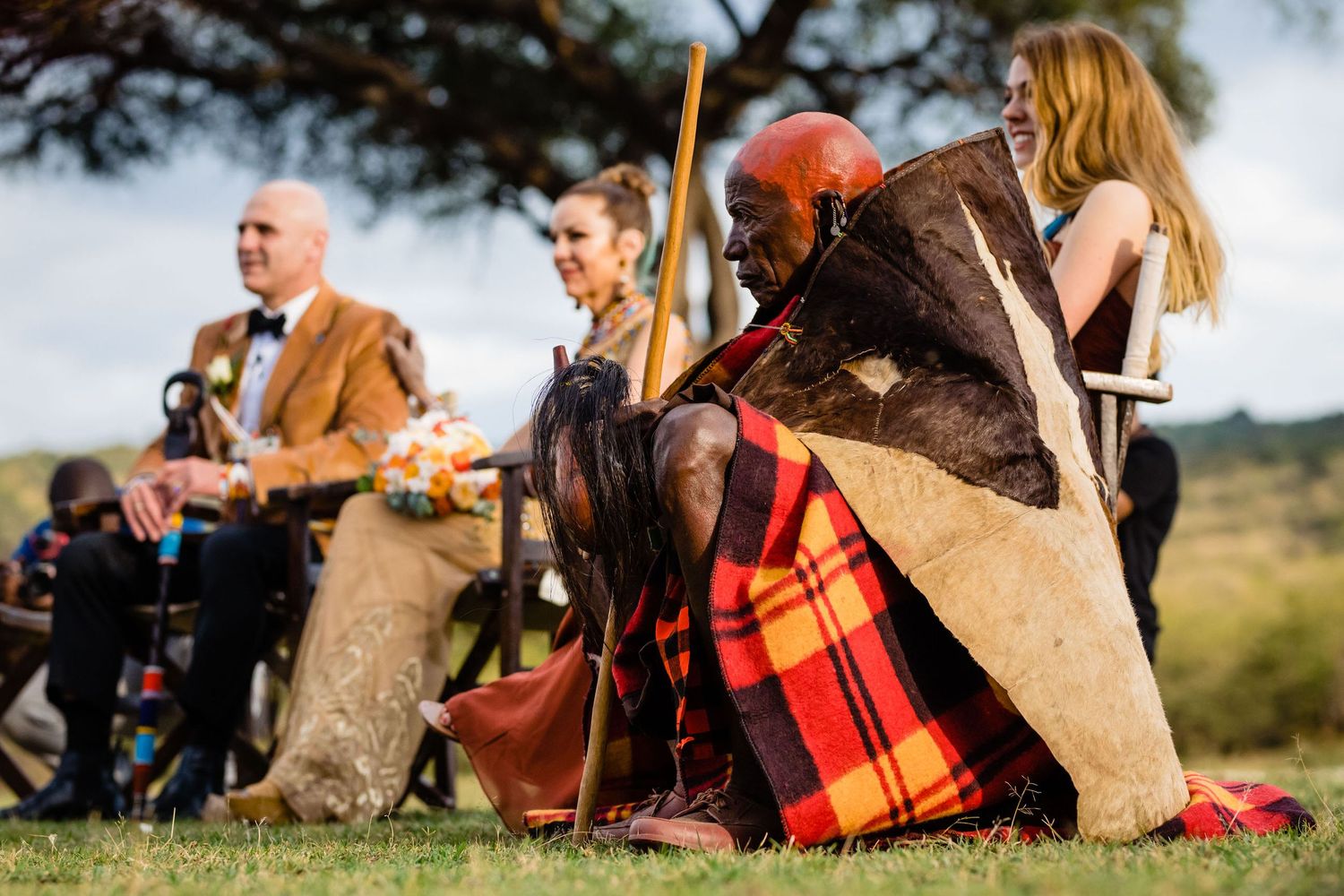 Wedding guests enjoy a picnic on blankets outdoors with colorful plaid throws.