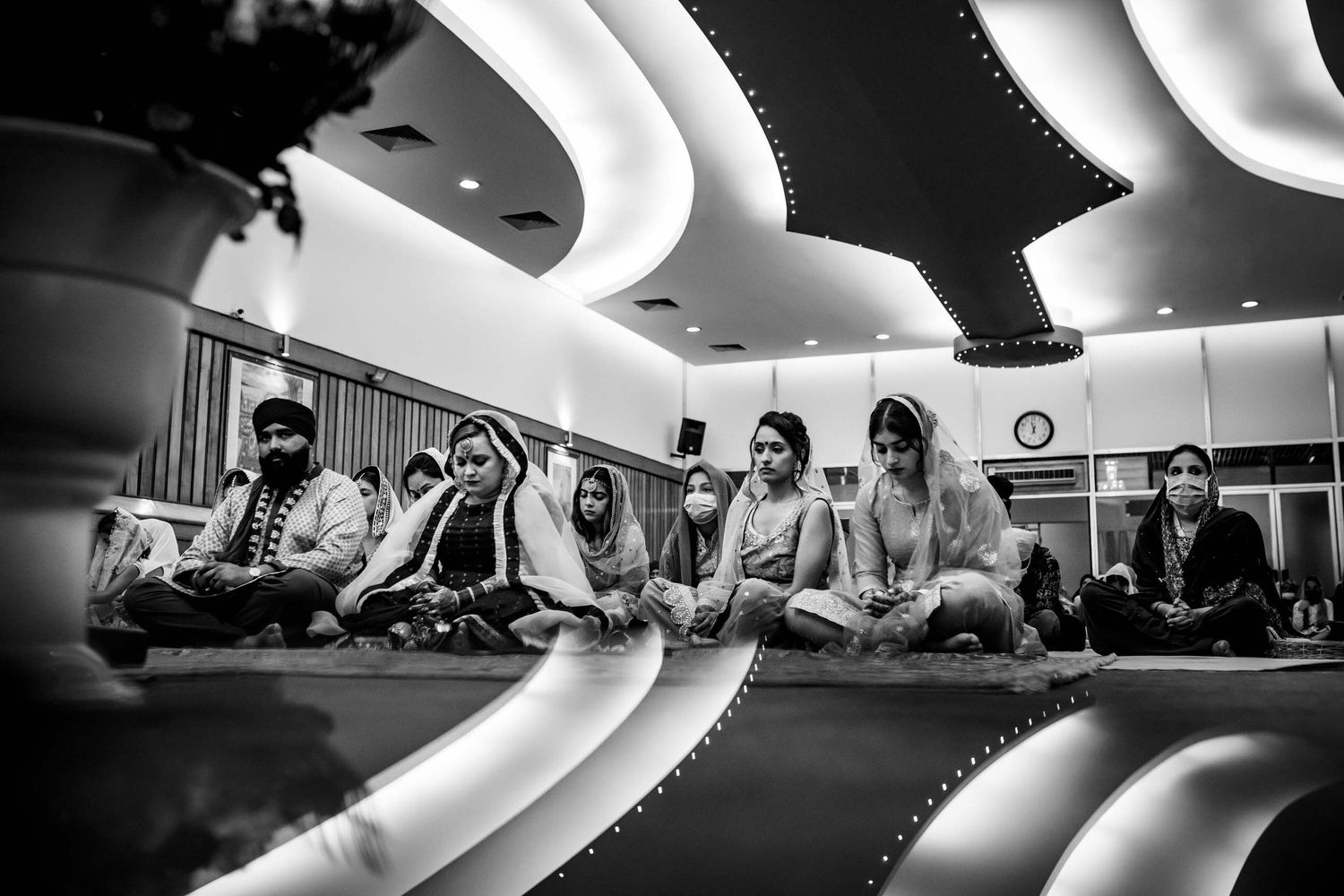 A group sits in meditation pose inside a modern room with curved white ceiling lights.