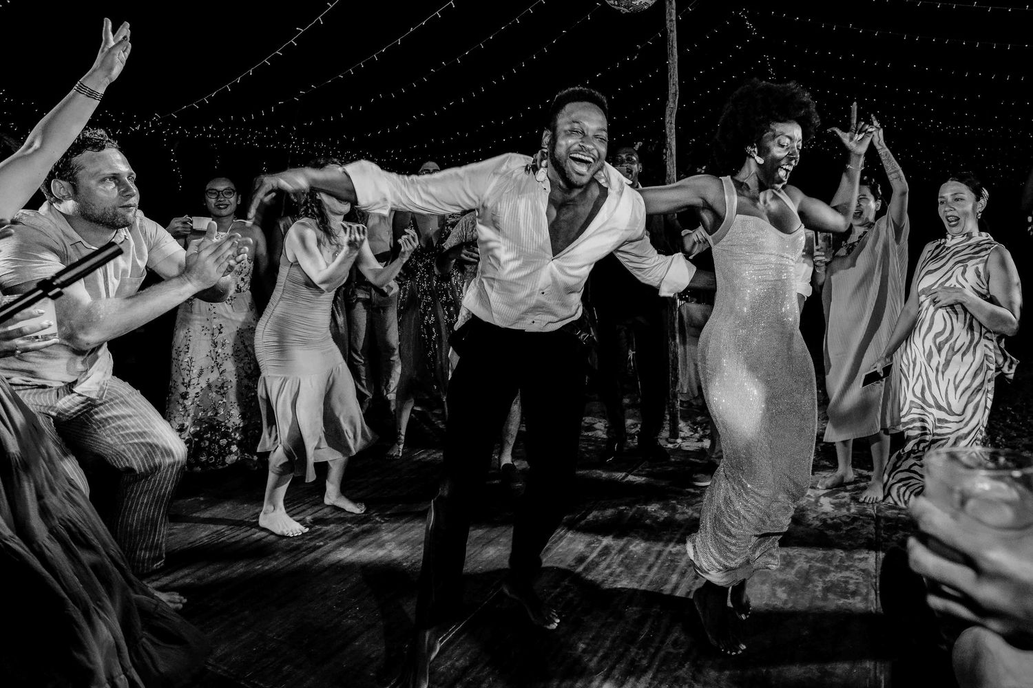 Wedding guests dance and celebrate on a dimly lit dance floor during an evening reception party.
