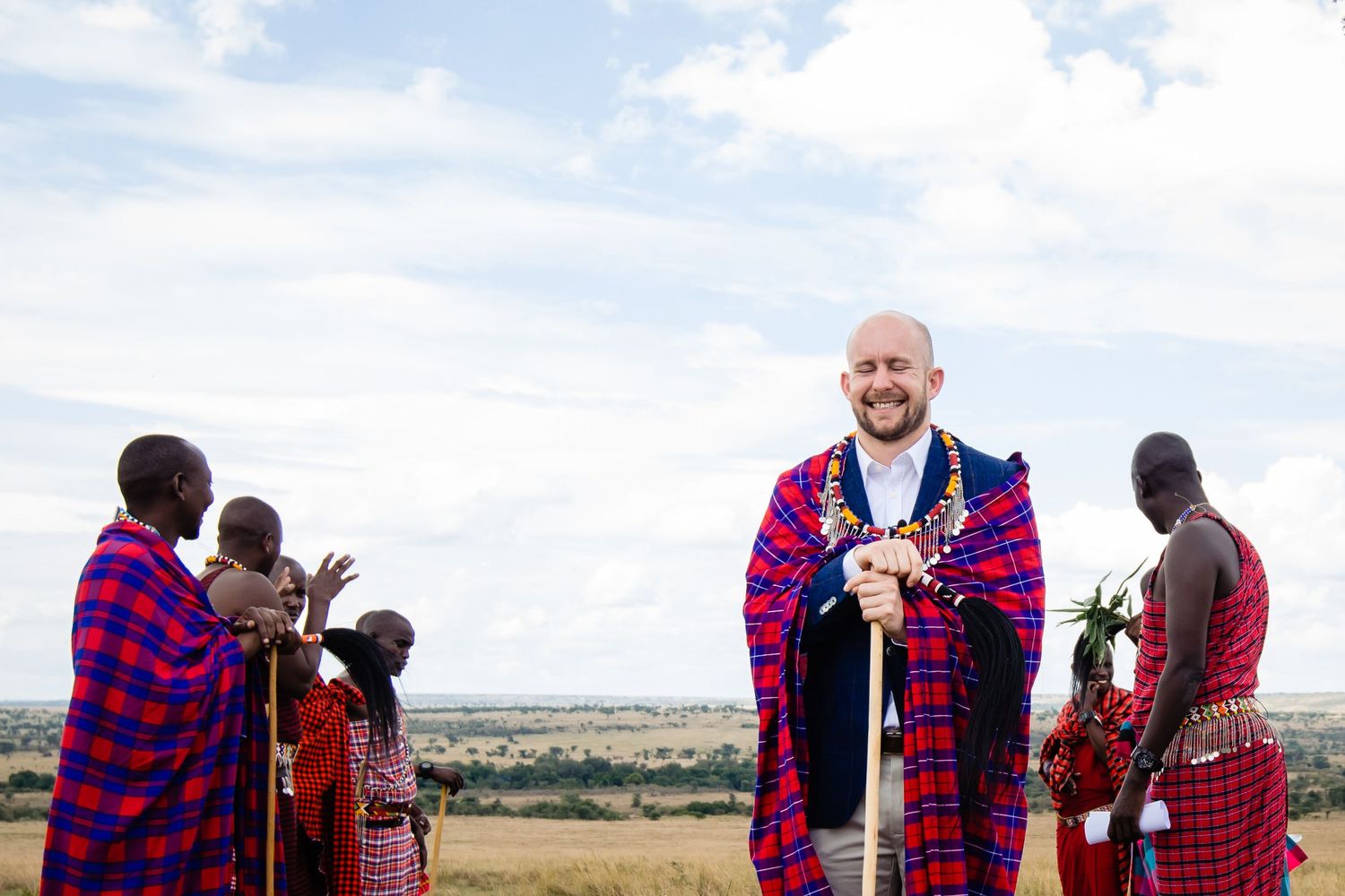 Group wearing traditional red and blue plaid Maasai clothing standing in an open field.